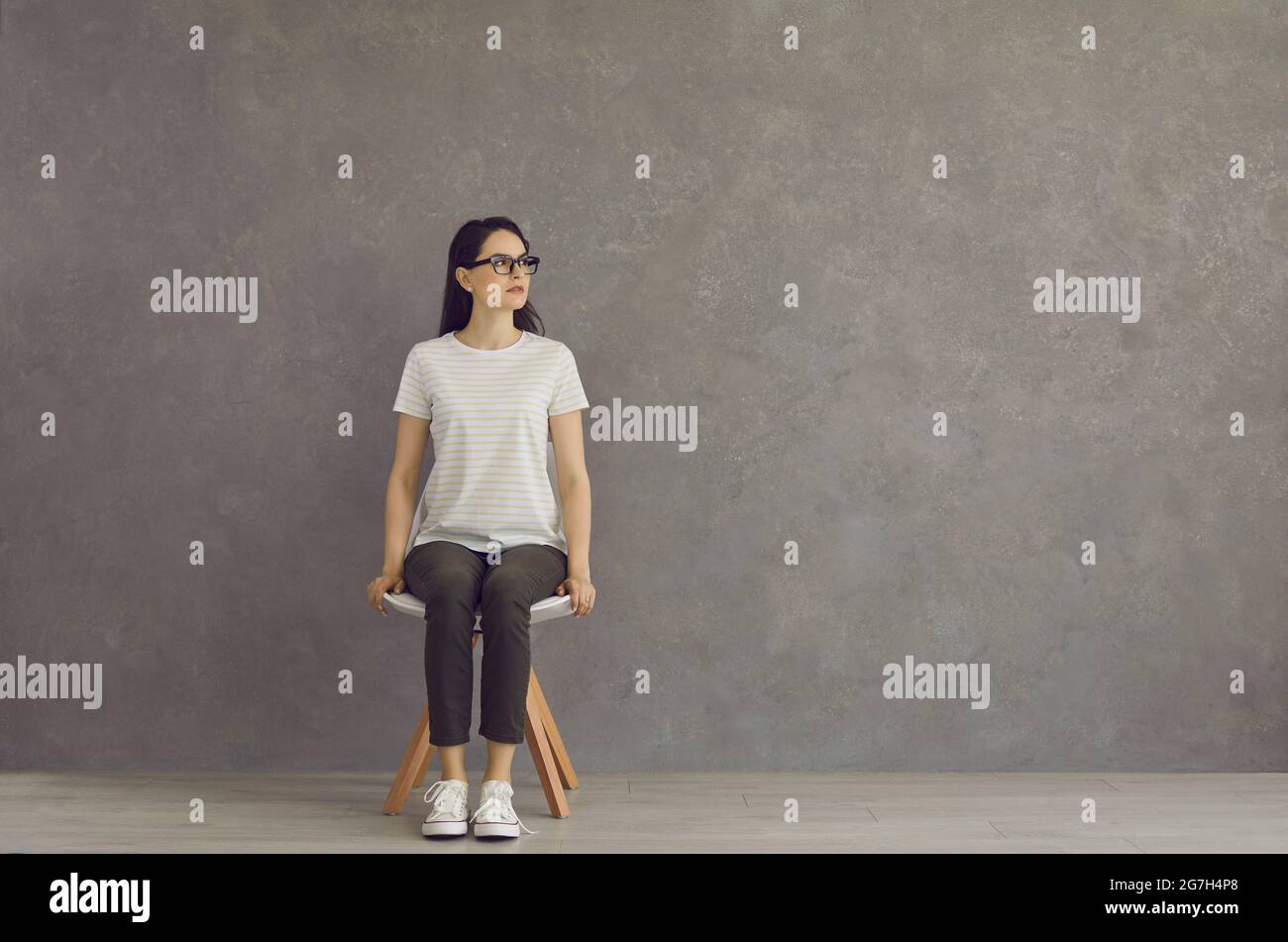 Ein junges, schönes Mädchen sitzt in vollem Wachstum auf einem weißen Hocker, in einem T-Shirt, Sportschuhen. Stockfoto