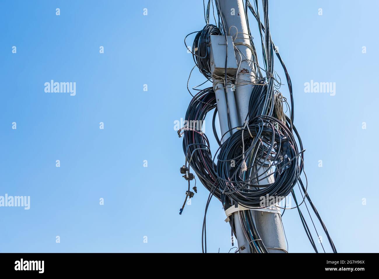 Viele Drähte für die Versorgung mit elektrischer Energie und Kommunikation verdreht um die Säule vor dem Hintergrund des Himmels Stockfoto