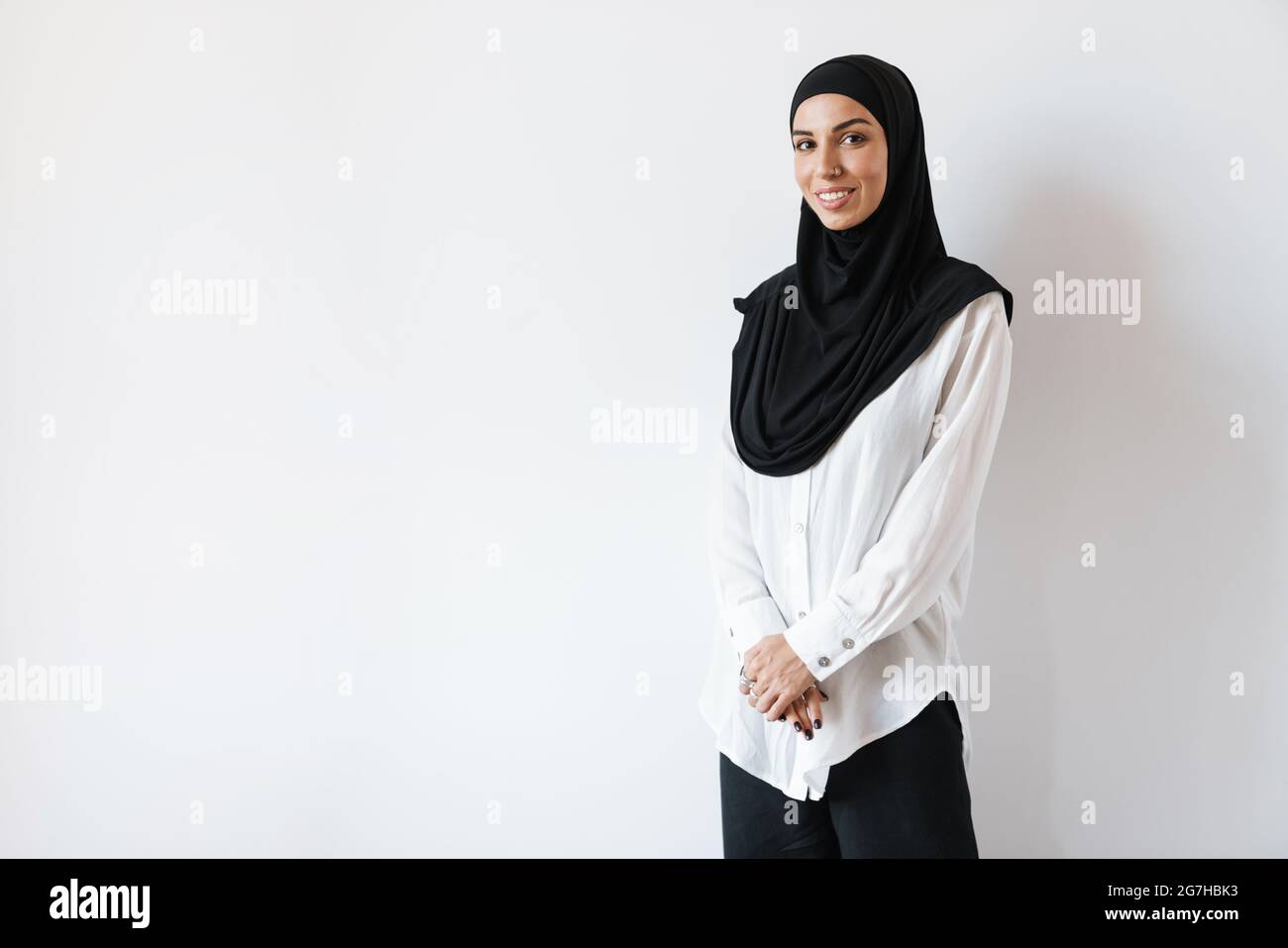 Eine lächelnde muslimische Frau im Hijab mit durchbohrter Nase, die im weißen Studio steht Stockfoto