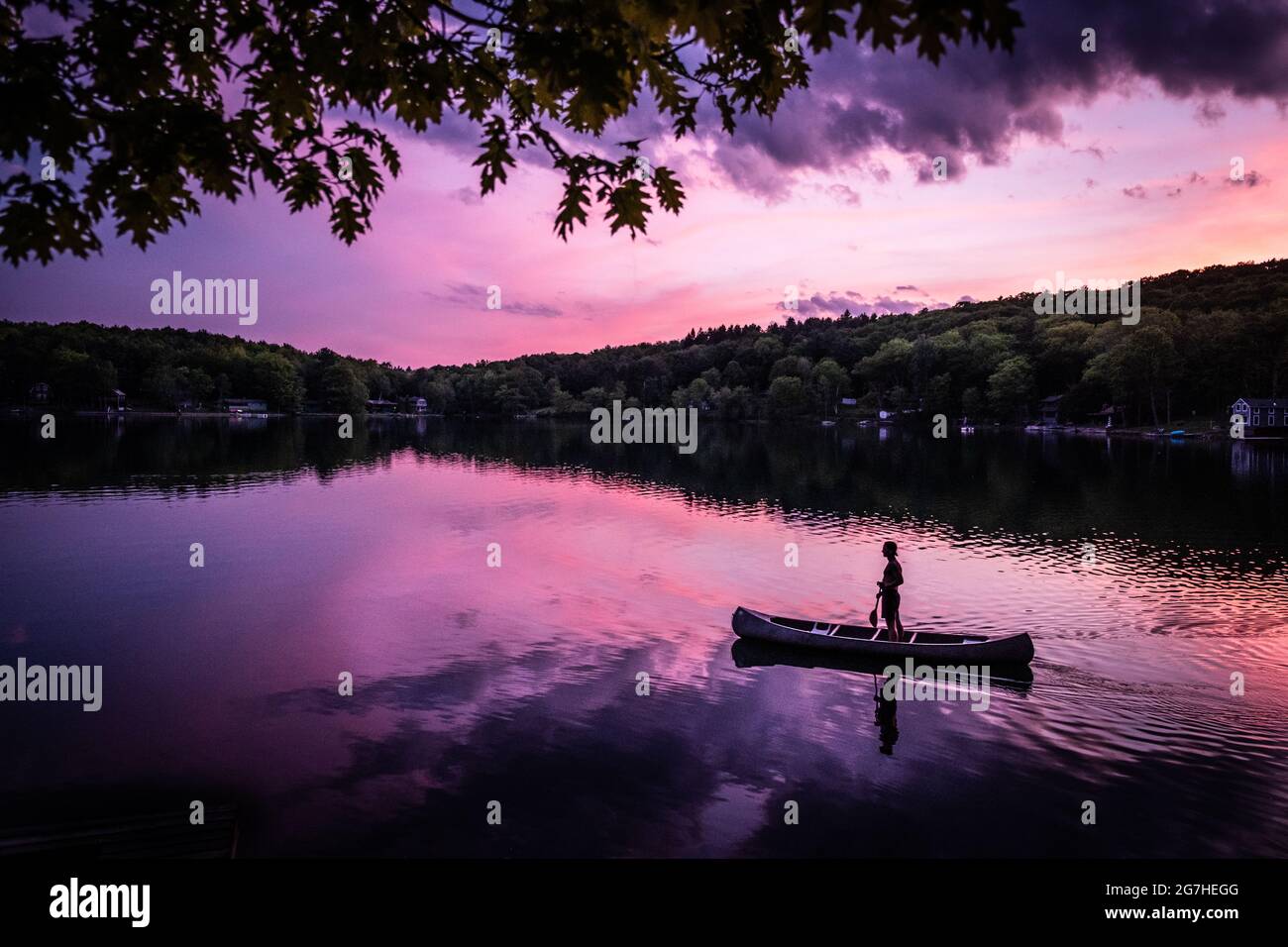 Kanufahrer steht im offenen Kanu auf, während sie bei Sonnenuntergang auf einem kleinen See in der Nähe von Cooperstown, NY, paddeln. Stockfoto