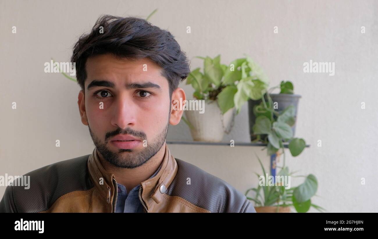 Junger indischer Mann mit brauner Lederjacke und Zimmerpflanzen im Hintergrund Stockfoto