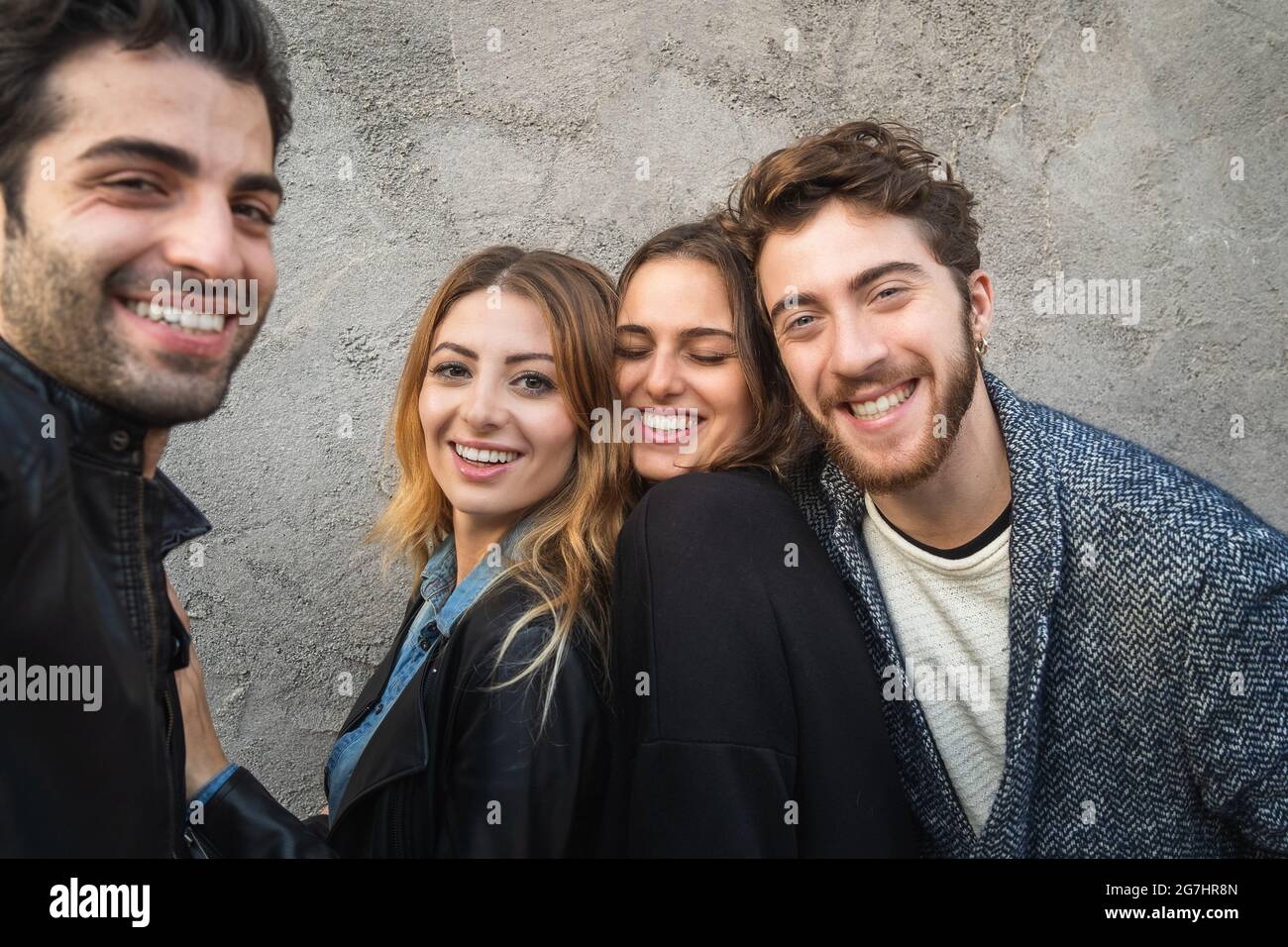 Porträt von Millennials, die die Kamera anlächeln. Eine Gruppe junger Leute, die sich gemeinsam an einer Betonwand amüsieren. Stockfoto