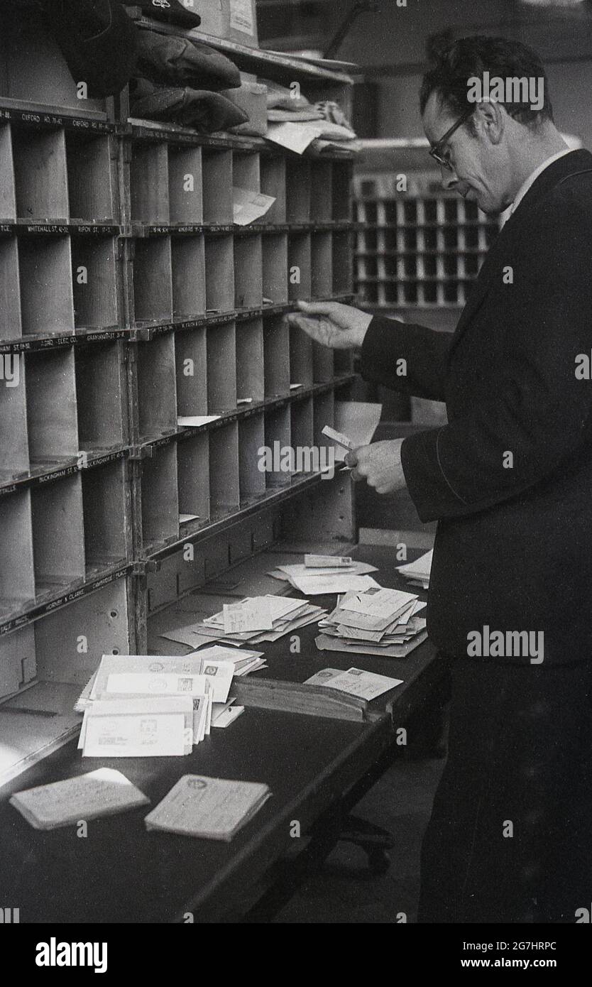In den 1950er Jahren, historisch, sortierte ein männlicher GPO-Arbeiter Briefe oder Post in den Kubby oder Taubenlöcher auf einem Holzregal für die verschiedenen Straßen des Bezirks, London, England, Großbritannien. Stockfoto