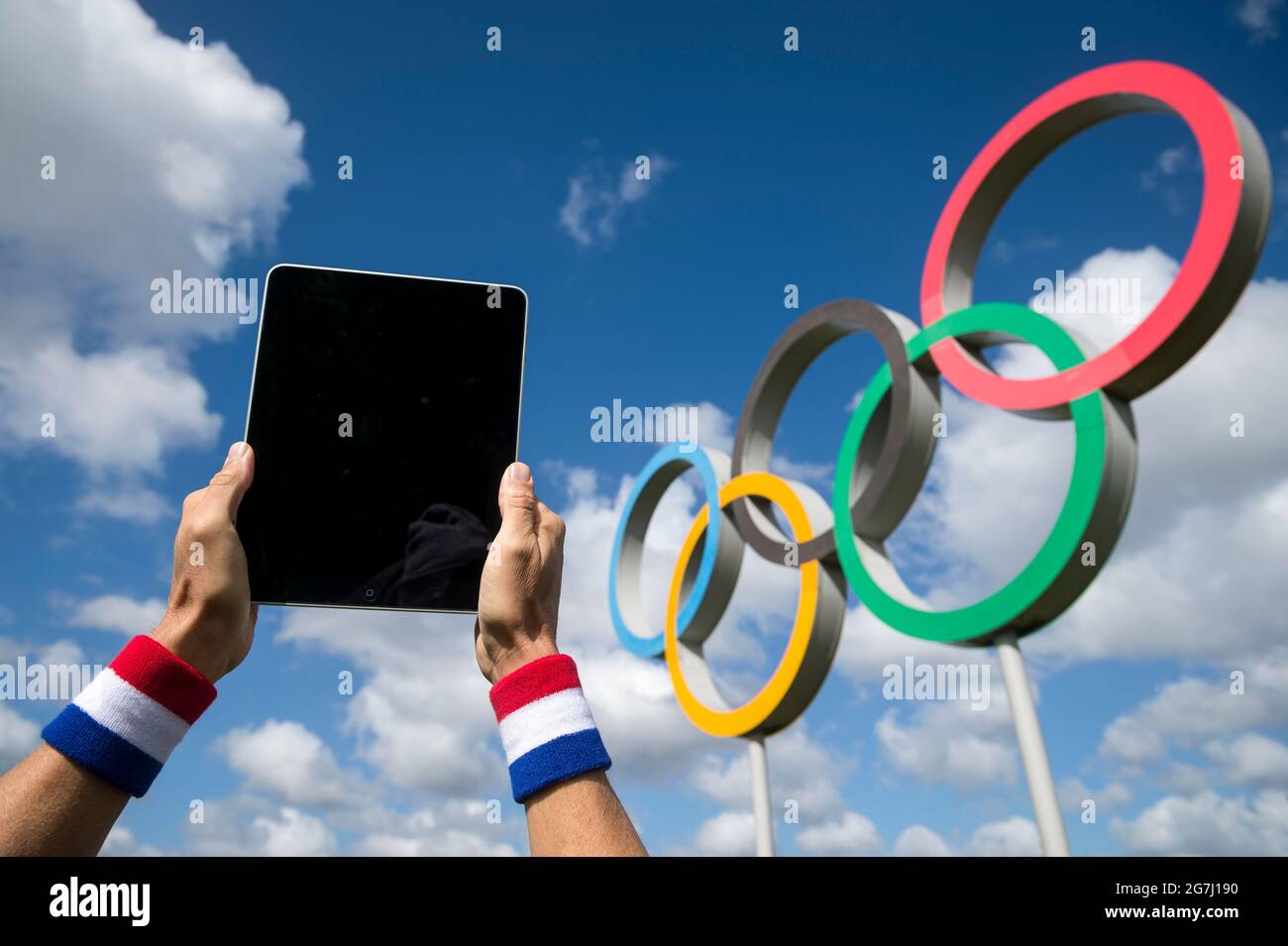 RIO DE JANEIRO - APRIL, 2016: Sportler mit einem rot-weißen und blauen Armband, der vor den Olympischen Ringen den Bildschirm eines Tablet-Computers berührt Stockfoto