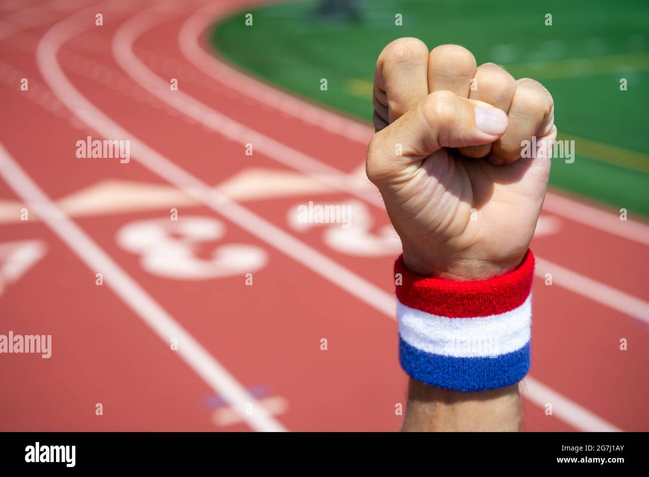 Sportler mit rotem, weißem und blauem Armband schlägt vor dem Hintergrund einer Sportstrecke in die Luft Stockfoto