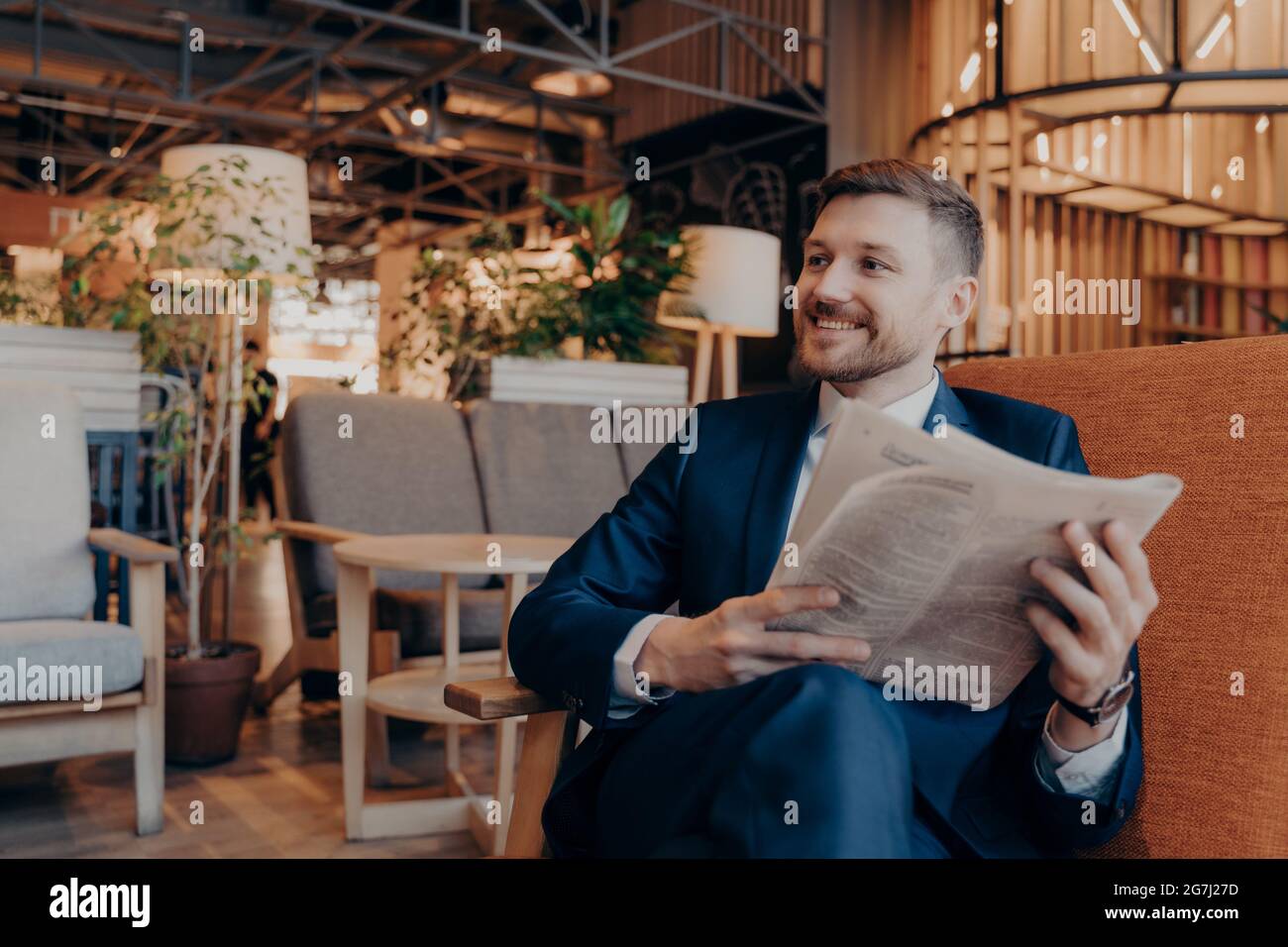 Positiver junger Geschäftsmann beim Lesen der Zeitung im Café Stockfoto