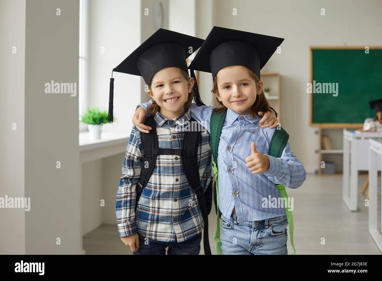 Porträt eines fröhlichen kleinen Studenten in Abschlusskappe, lächelnd an die Kamera umarmt Stockfoto