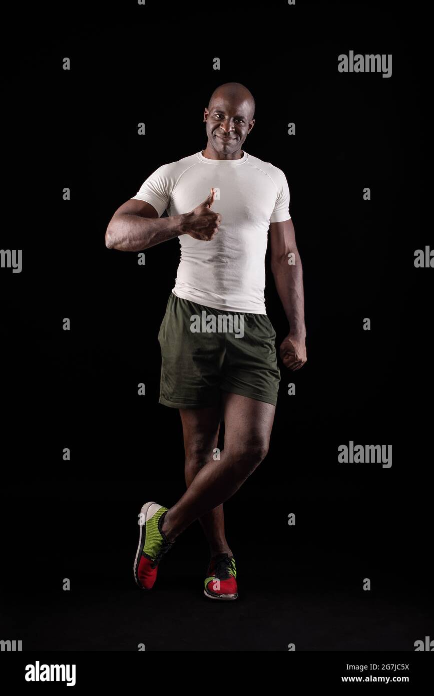 Schwarzer Mann, der mit dem Daumen nach oben und einem gekreuzten Bein auf die Kamera schaut Stockfoto