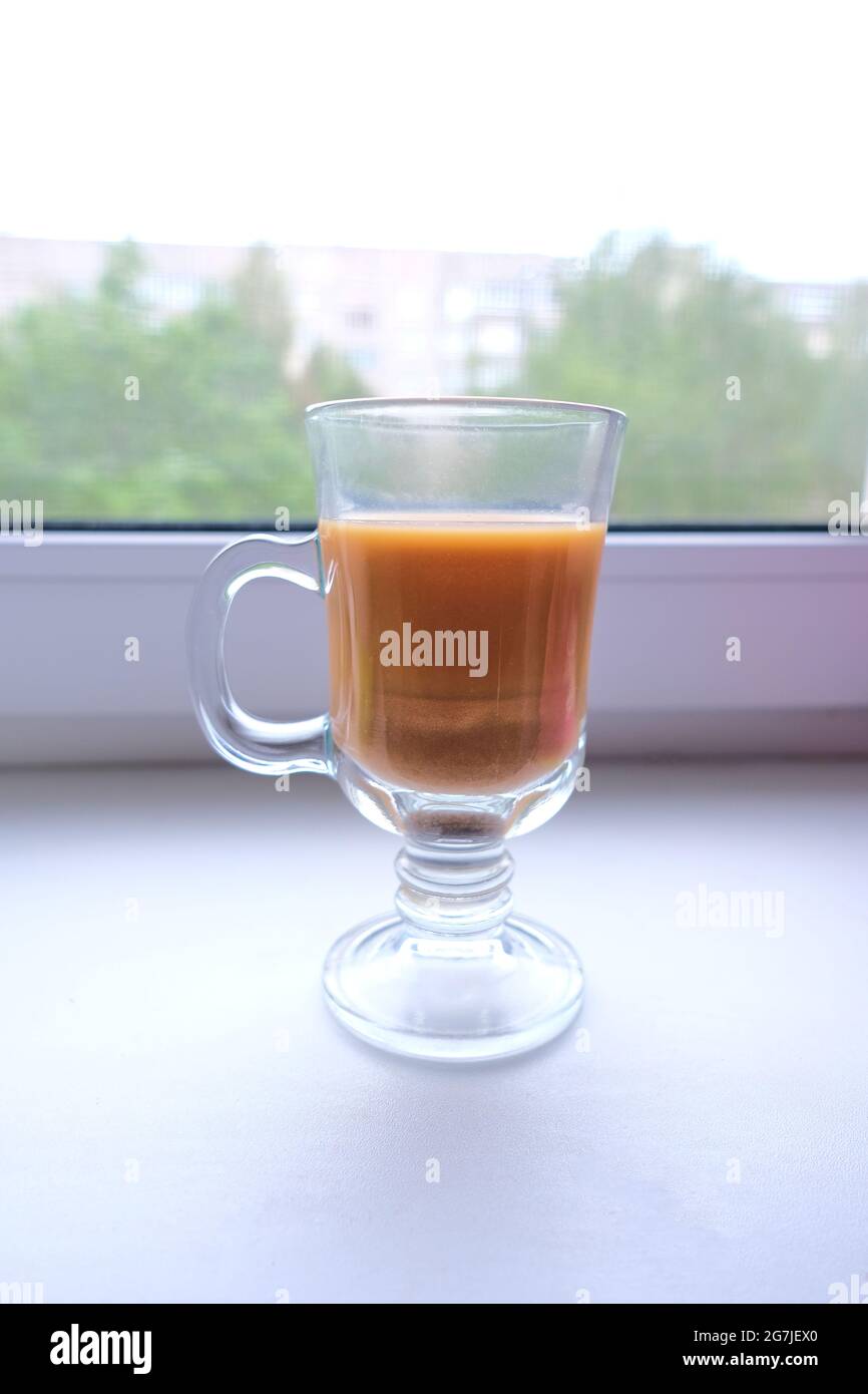 Kaffee mit Milch in einer transparenten Tasse auf der Fensterbank Stockfoto