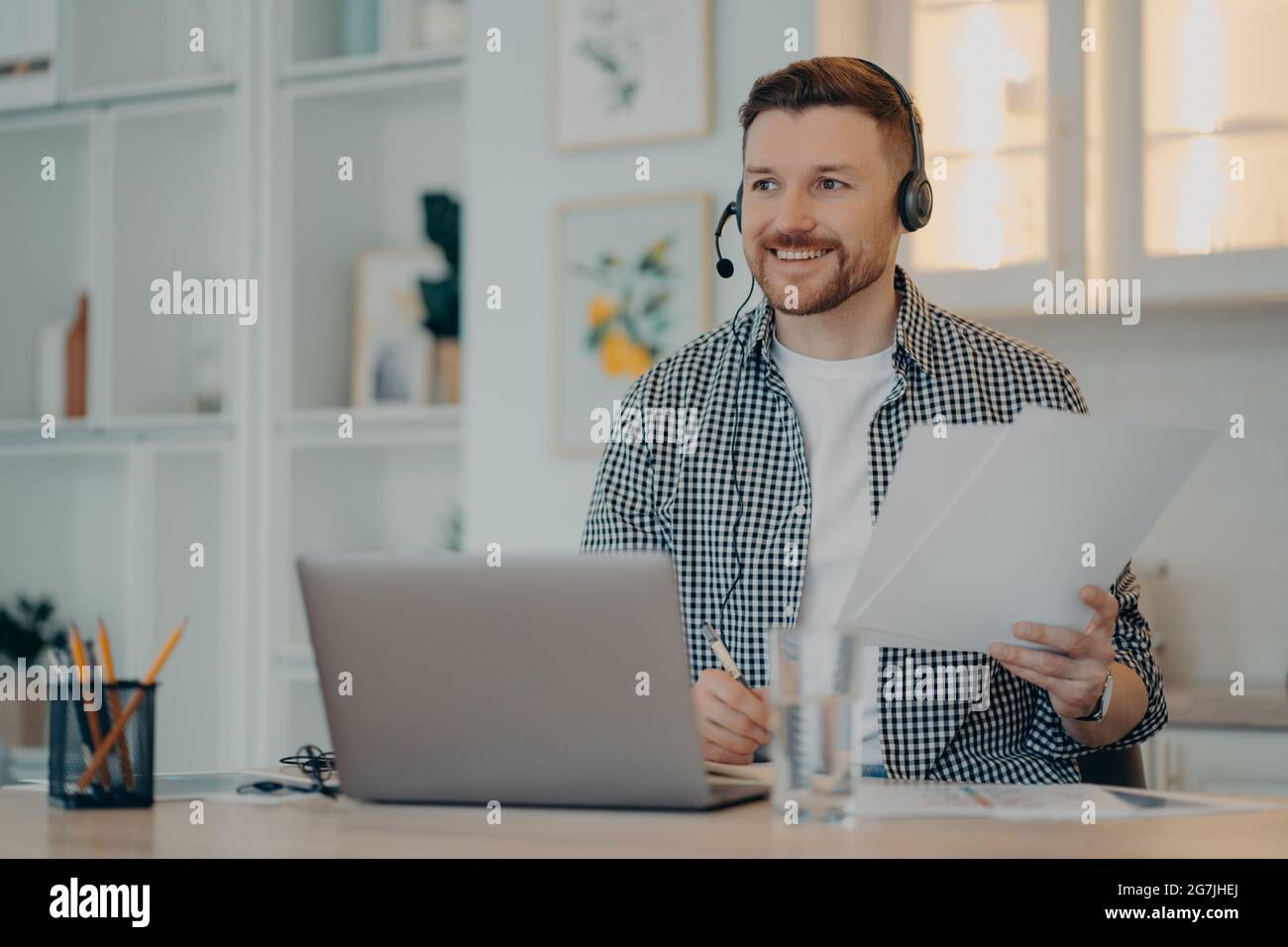 Glücklicher Mann, der während eines Online-Anrufs zu Hause Papiere hält Stockfoto