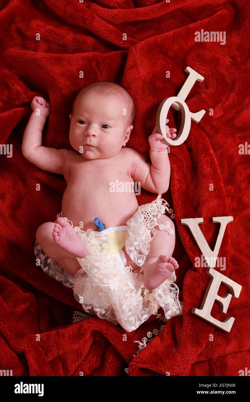 Neugeborener Junge mit umbilischer Kordelklemme, die im Kinderzimmer noch auf einer roten Decke befestigt ist Stockfoto