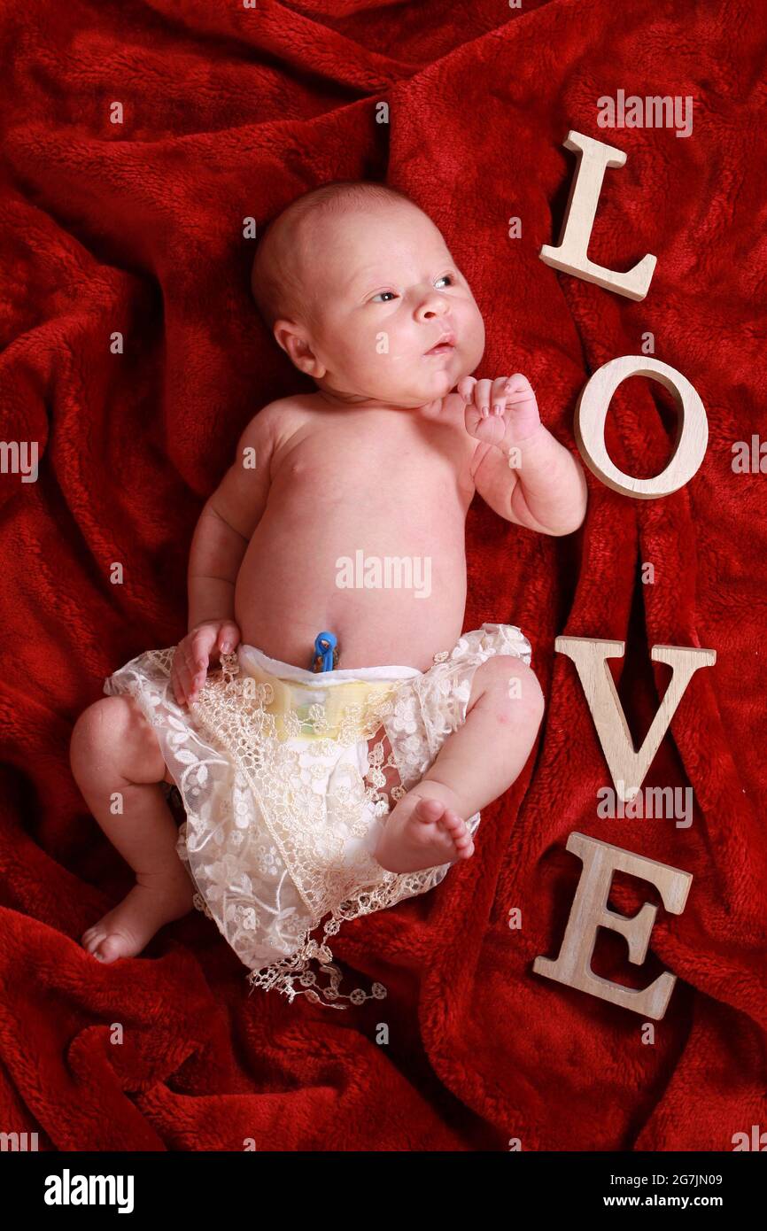 Neugeborener Junge mit umbilischer Kordelklemme, die im Kinderzimmer noch auf einer roten Decke befestigt ist Stockfoto