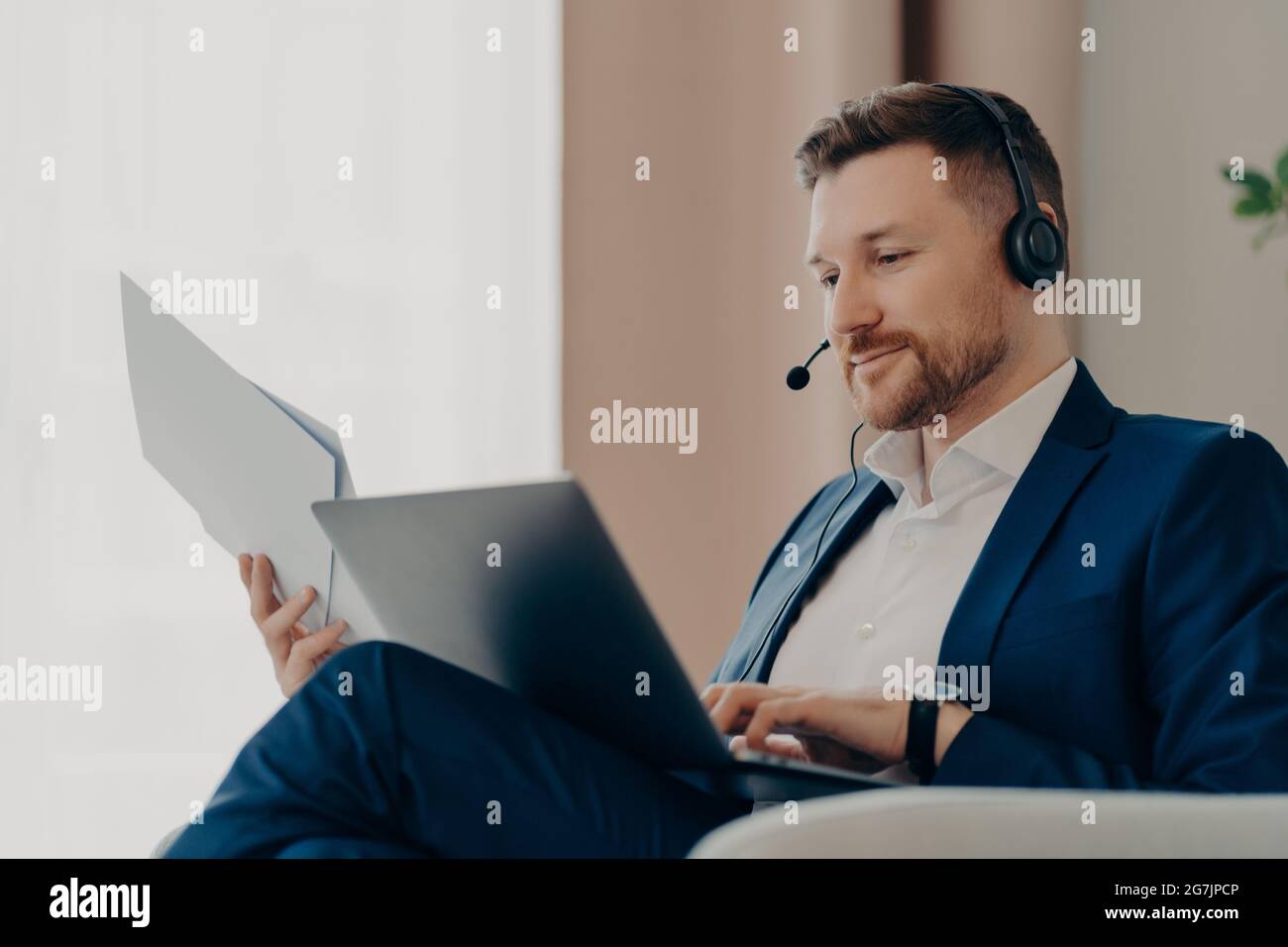 Nachdenklicher Geschäftsmann, der zu Hause mit Online-Projekten arbeitet und dabei Papiere hält Stockfoto