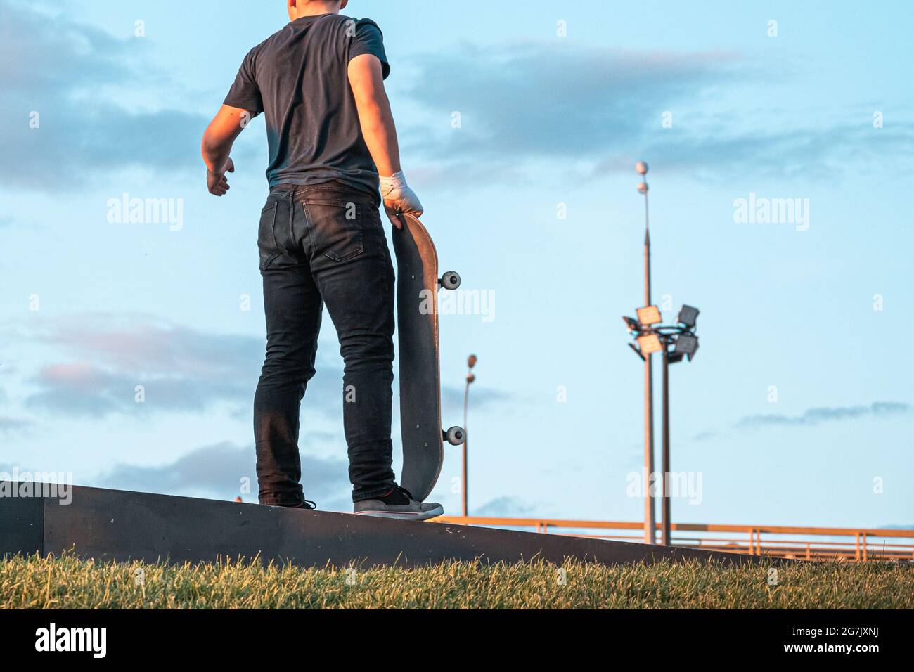 Ein Fahrer mit einer bandagierten Hand und einem Skateboard steht neben der Rampe in einem Skatepark. Sport, Extremsport, Skateboarding, das Konzept der aktiven r Stockfoto