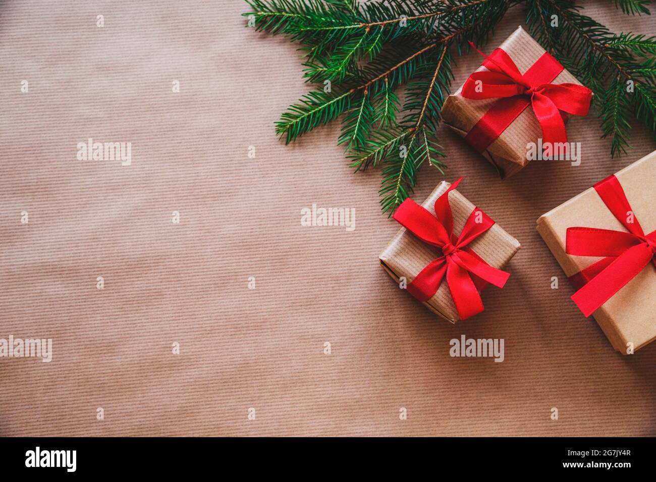 Hintergrund zu Weihnachten und Neujahr. Christbaumzweige, Geschenkschachteln mit rotem Band auf Bastelpapier-Hintergrund. Draufsicht, flach liegend, Copy Spa Stockfoto