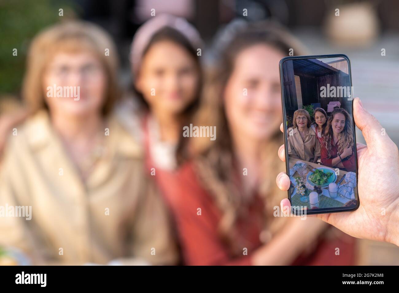 Hände eines Mannes, der das kleine Mädchen, ihre Mutter und Großmutter fotografiert, Fokus auf Bildschirm, Stockfoto