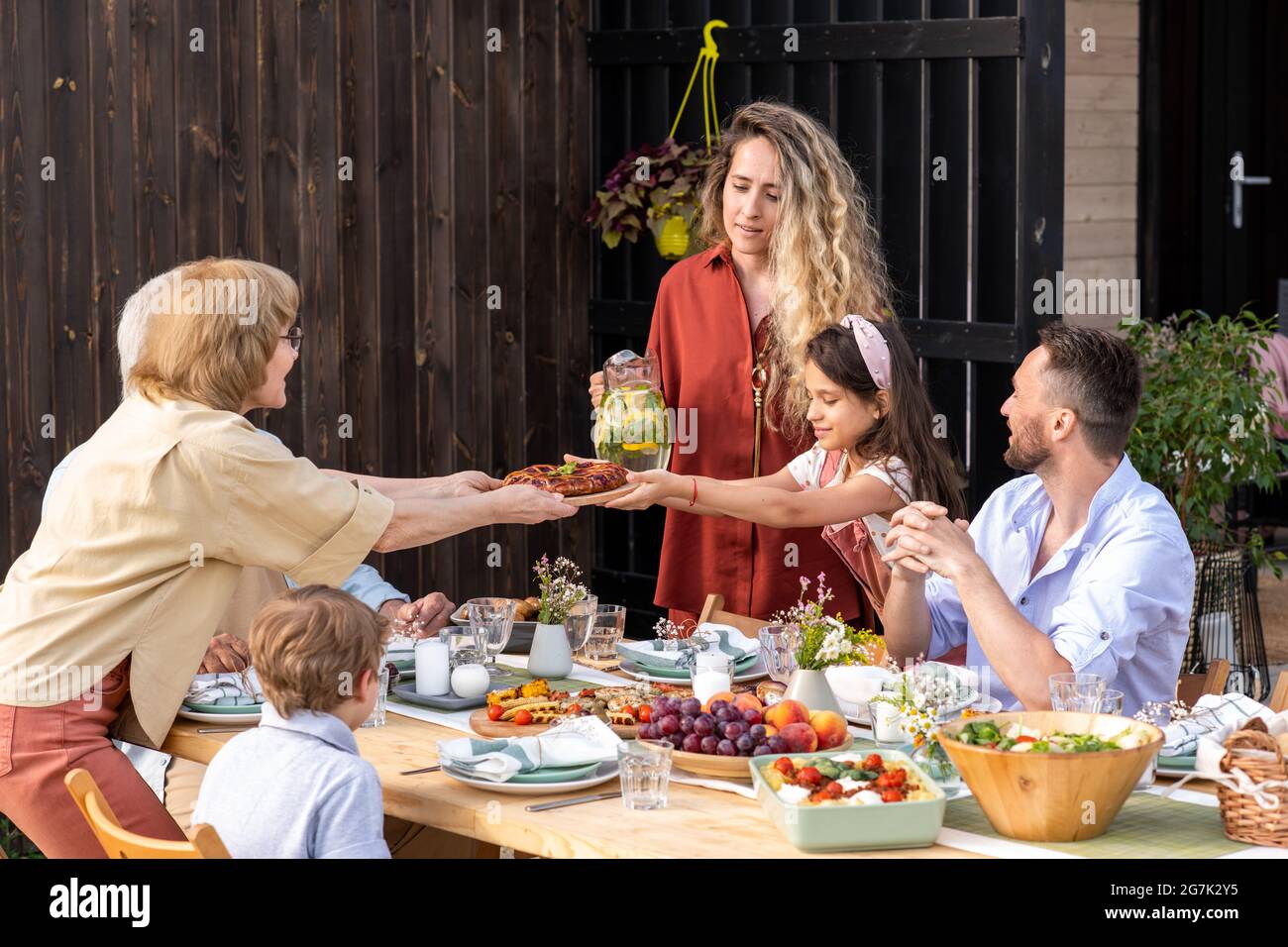 Große Familie genießt leckeres Abendessen am Tisch im Hinterhof, Granmother Weitergabe Kirschkuchen an Enkelin Stockfoto