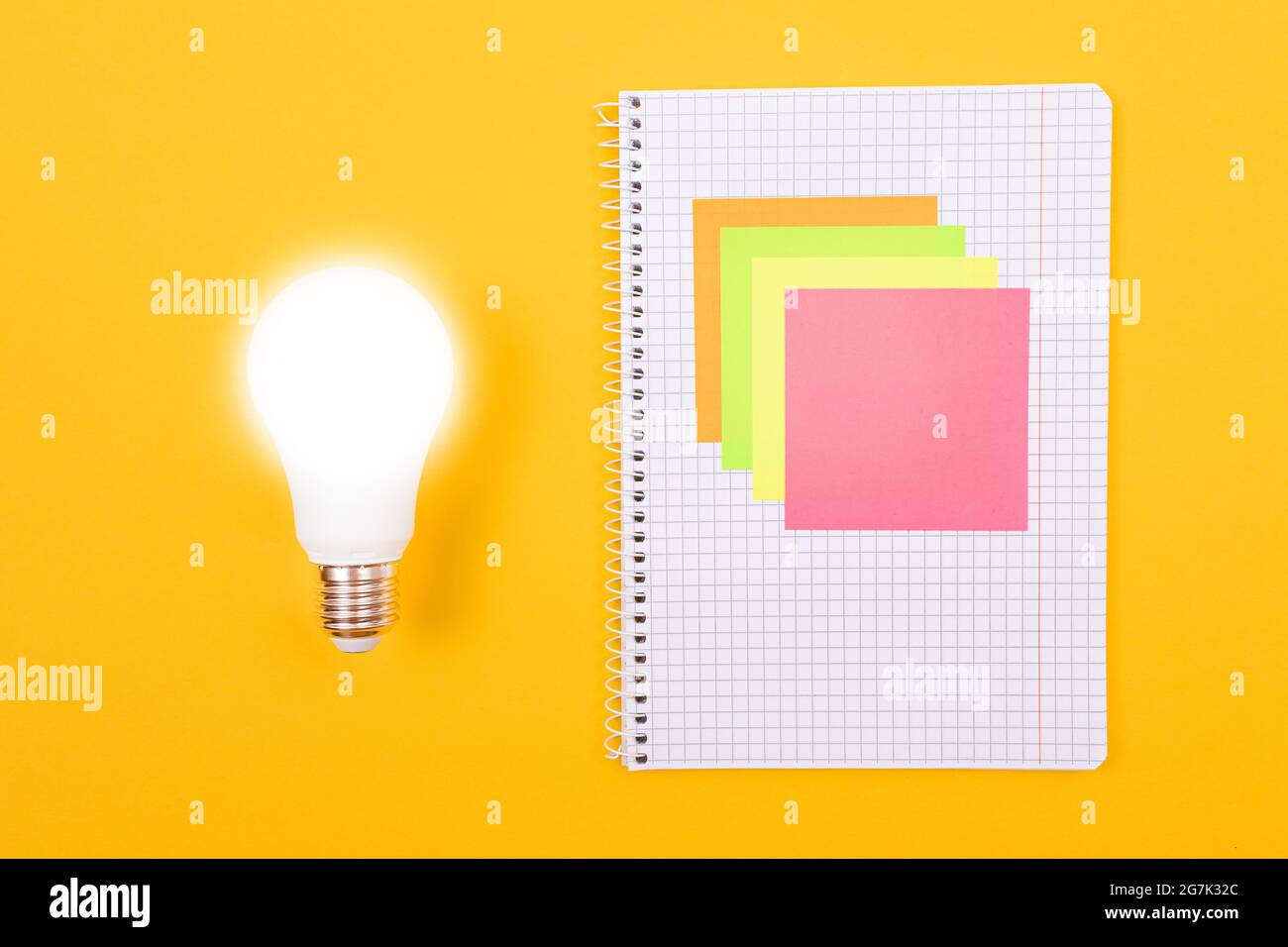 Ein Ideenkonzept - leuchtende Energiesparlampe und EIN Notizblatt mit Haftnotizen auf gelbem Tisch. Draufsicht, Flach Liegend, Leere Vorlage Stockfoto