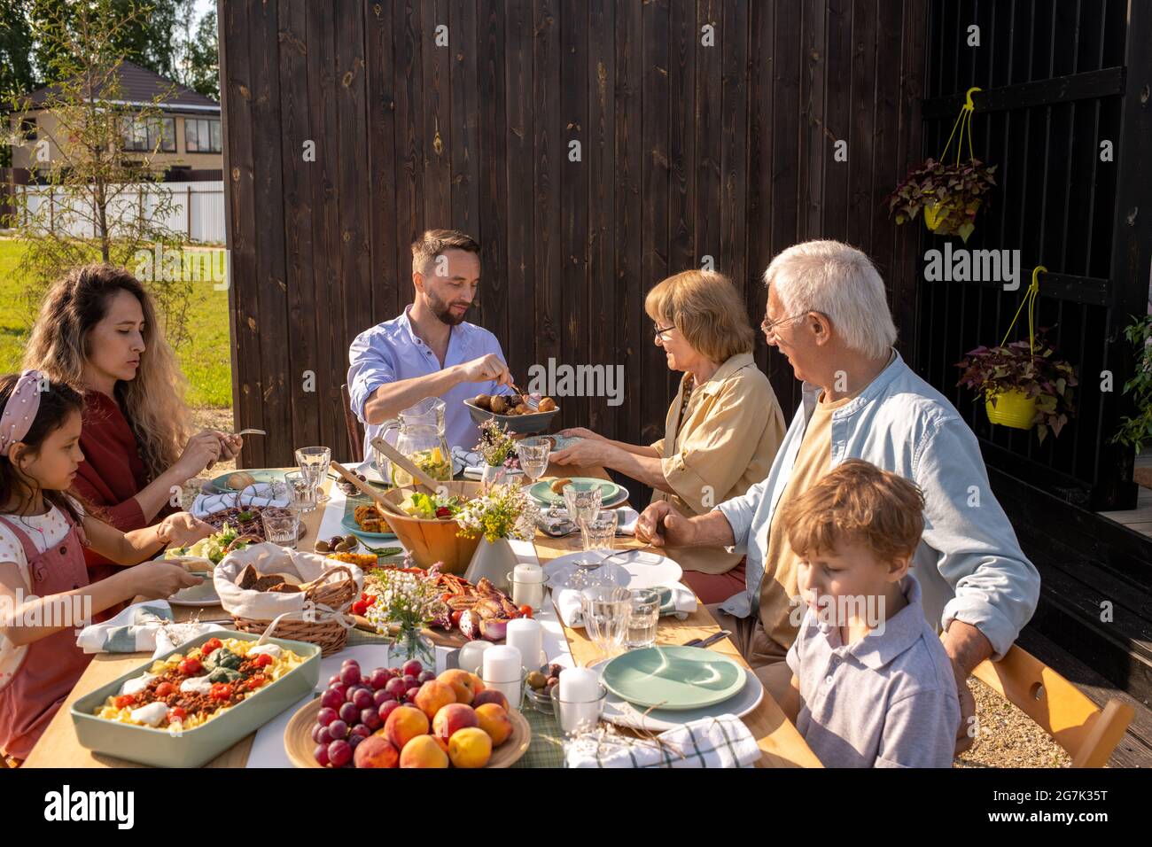 Große Familie essen leckeres Essen an einem großen Tisch im Hinterhof des Ferienhauses am sonnigen Sommertag Stockfoto