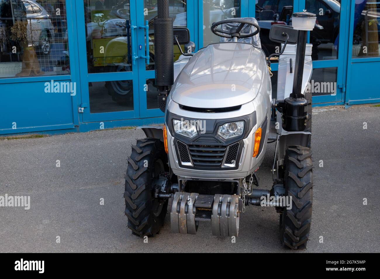Neuer Mini-Traktor auf dem Parkplatz am Eingang zum Bauernmarkt, Ausrüstung für landwirtschaftliche Arbeit. Stockfoto
