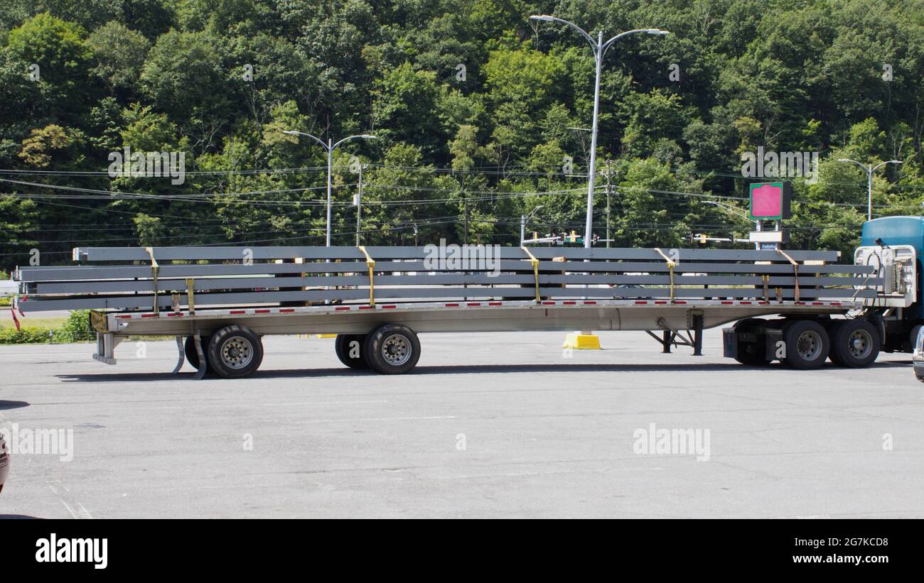 Seitenansicht eines Flachbett-Anhängers mit großen Stahlträgern auf dem Transport Stockfoto