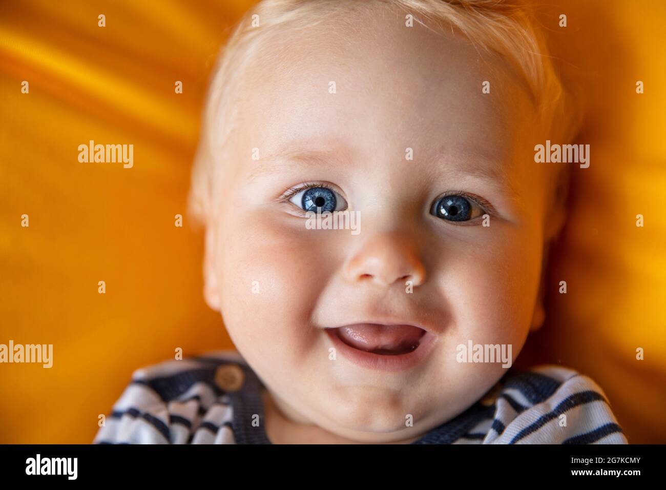 Nahaufnahme eines niedlichen 9 Monate alten Jungen mit blauen Augen auf einem gelben Hintergrund Stockfoto