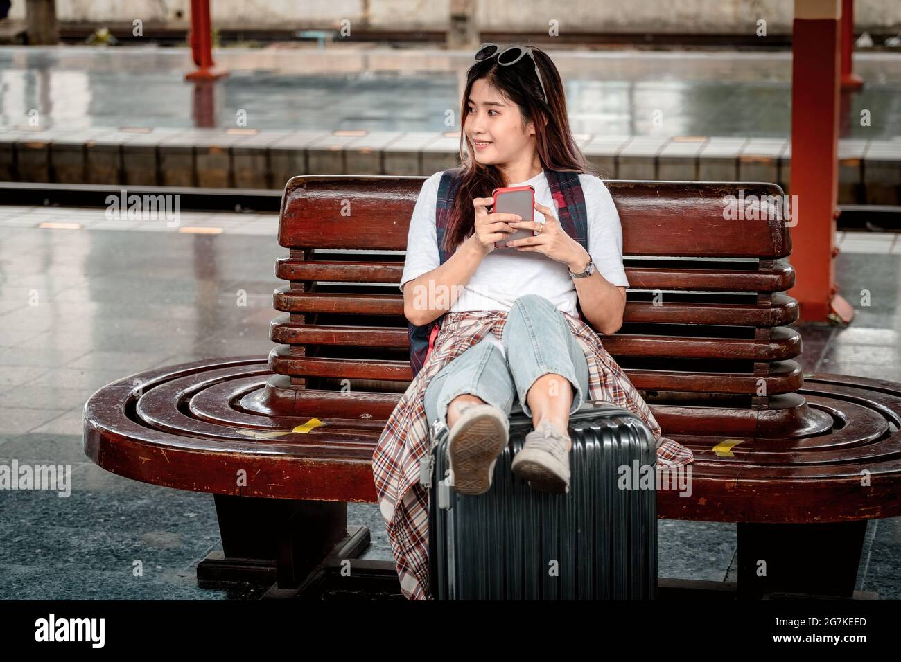 Junge Hipster-Frau wartet auf der Bahnhofsplattform mit Rucksack. Reisekonzept. asiatisches Mädchen mit Smartphone am Bahnhof Stockfoto