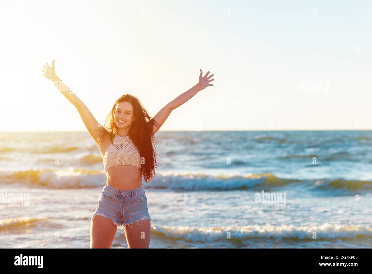 Schöne sexy Mädchen heben die Hände auf dem Meer Strand in einer lässigen Kleidung schaut auf die Kamera bei Sonnenuntergang. Nahaufnahme eines modischen Mädchen.schönes Porträt von Stockfoto