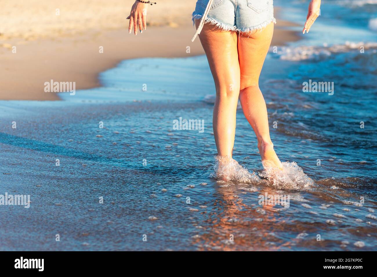 Frau Beine und Füße, die auf dem Sand des Strandes mit dem Meerwasser im Hintergrund zu Fuß auf dem Strand. Nahaufnahme von Beinen, die am Meer entlang laufen Stockfoto