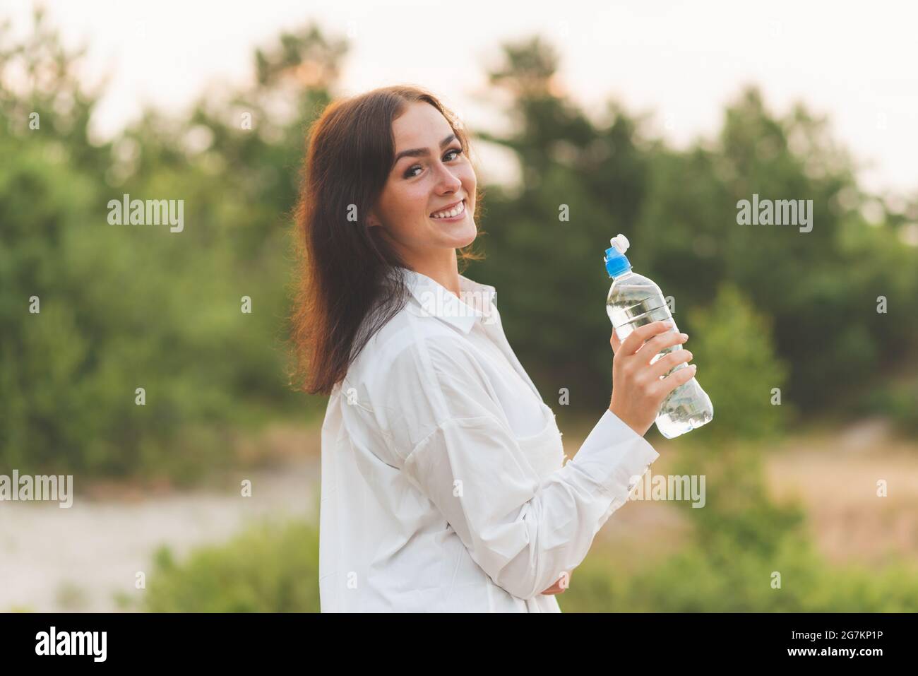 Mädchen trinkt Wasser aus einer Plastikflasche. Junge kaukasische Frau im Naturwald in Wäldern, während sie eine Flasche Wasser hält, die eine Bremse nimmt und eine Pause tra hat Stockfoto