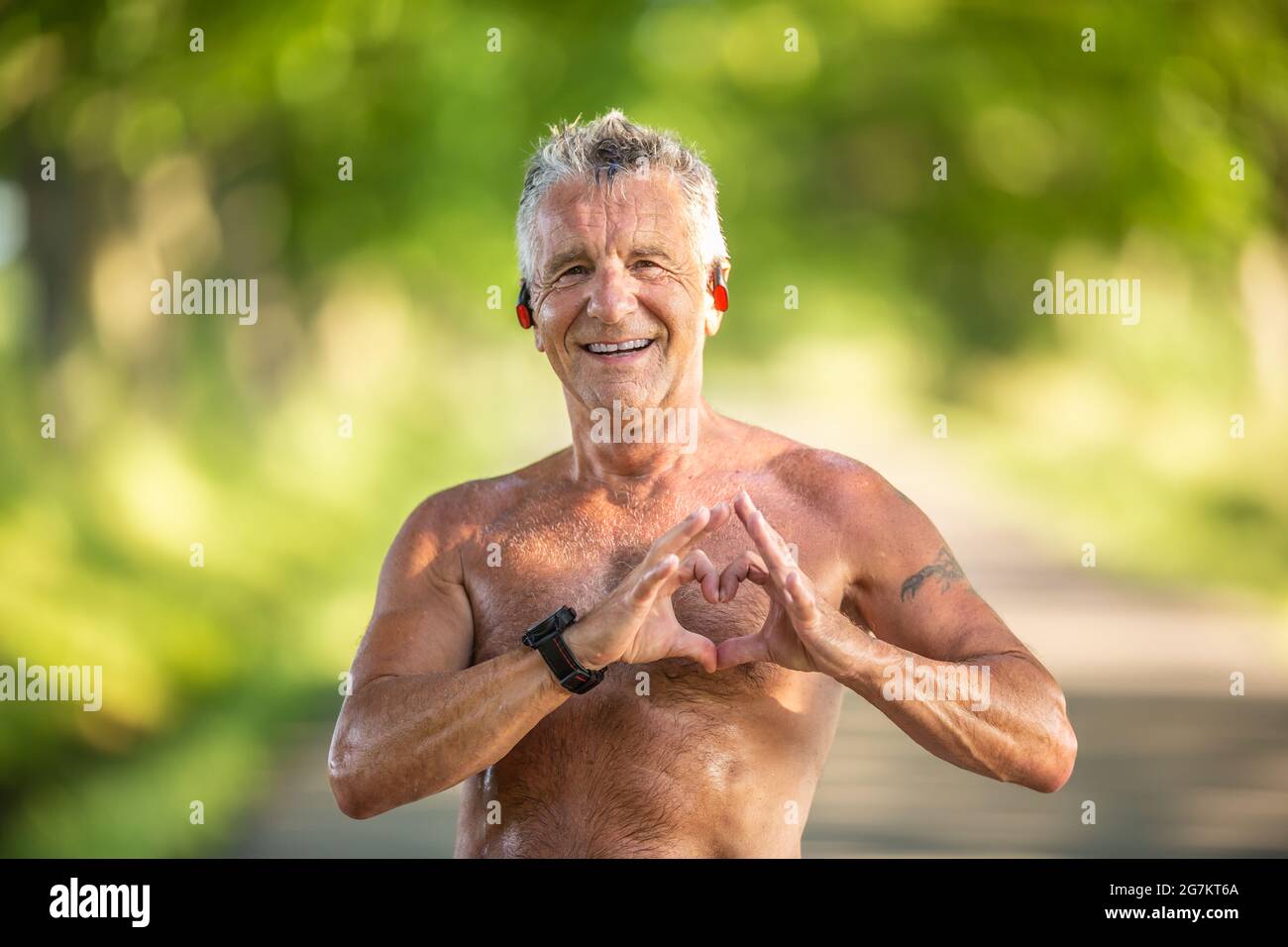 Ein alter, aber falter Mann mit grauem Haar zeigt mit den Fingern eine Herzbewegung als Zeichen seines gesunden Herz-Kreislauf-Systems. Stockfoto