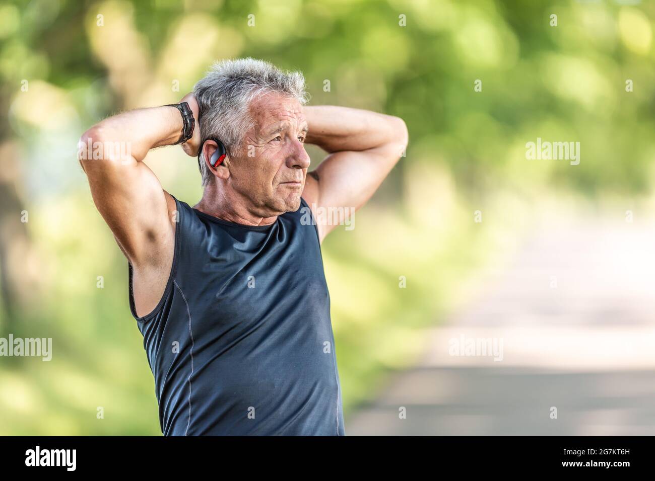 Der ältere Mann legt sich nach einem Lauf im Freien entspannt mit den Händen hinter die Hände. Stockfoto