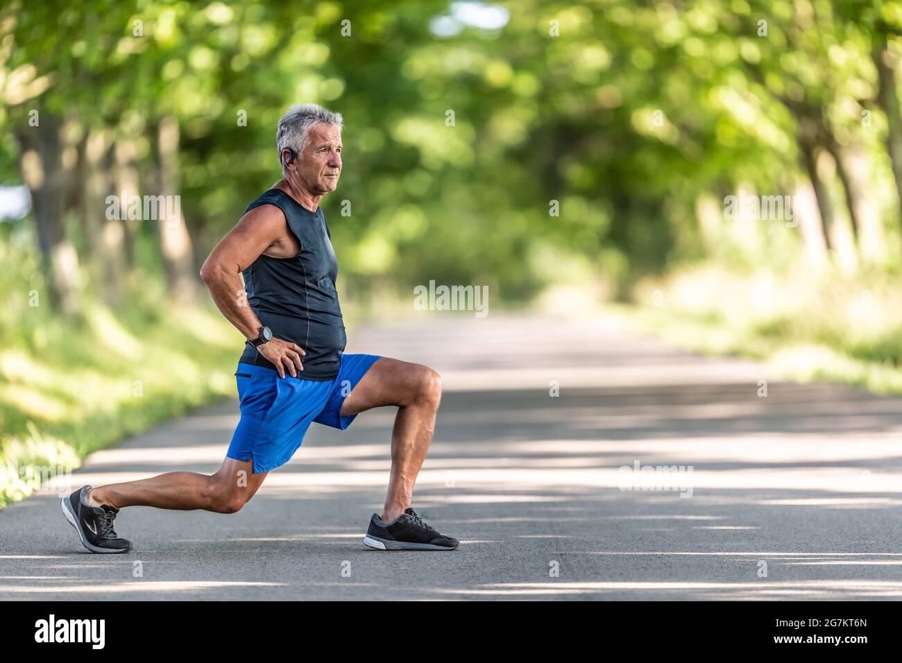 Gealterter Mann streckt vor seinem Training die Beine im Freien, umgeben von Bäumen. Stockfoto