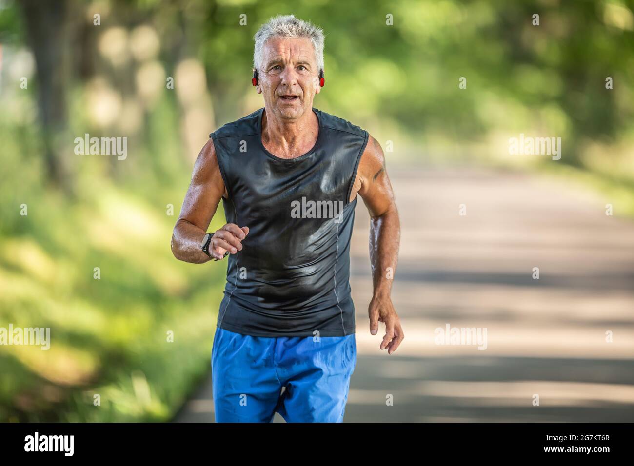 Muskulöser älterer Mann in guter Verfassung läuft im Freien und schwitzt während eines Laufs mit angeschrauben Kopfhörern. Stockfoto