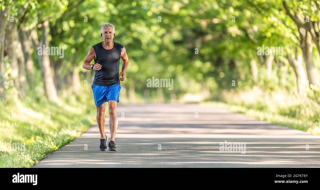 Der ältere Mann läuft an einem Sommertag bergauf in der Natur und hält sein Fitnessniveau hoch. Stockfoto