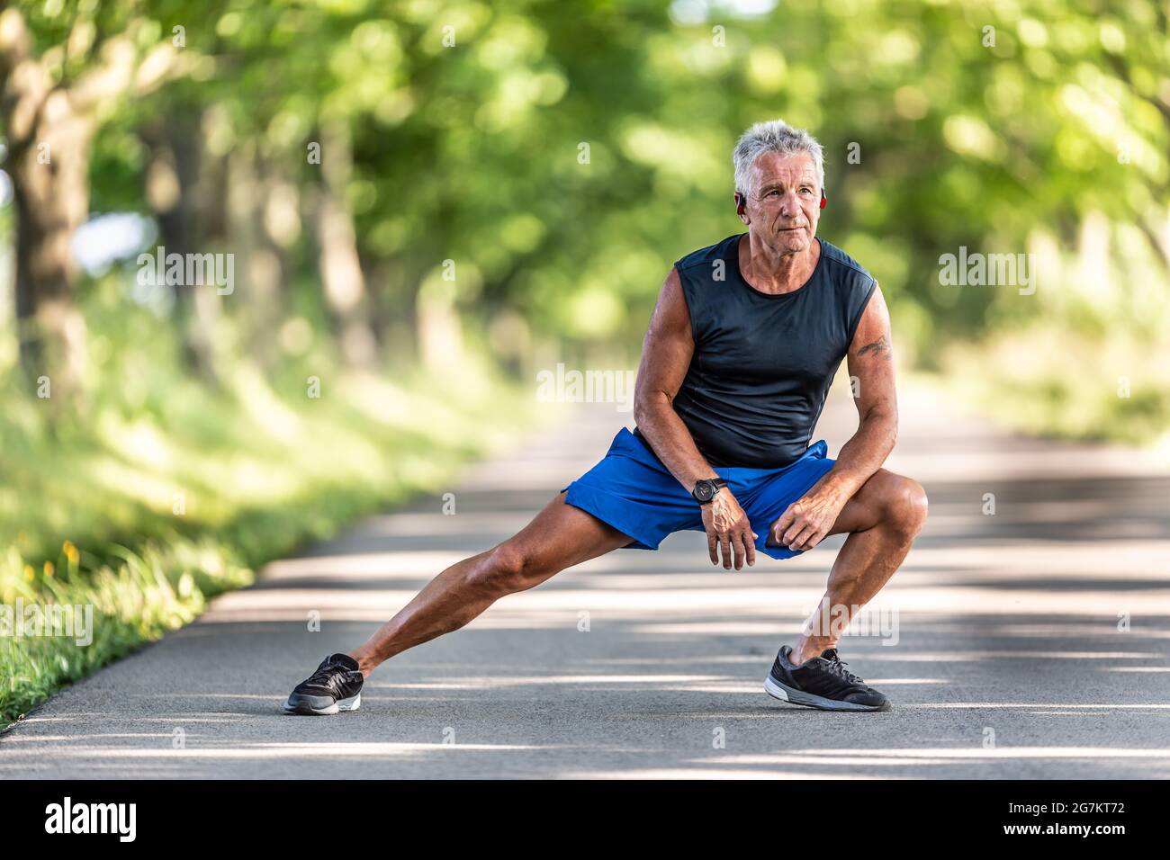 Der grauhaarige alte Mann, der noch in Form ist, streckt die Beine in seinem Aufwärmpuls vor dem Training. Stockfoto