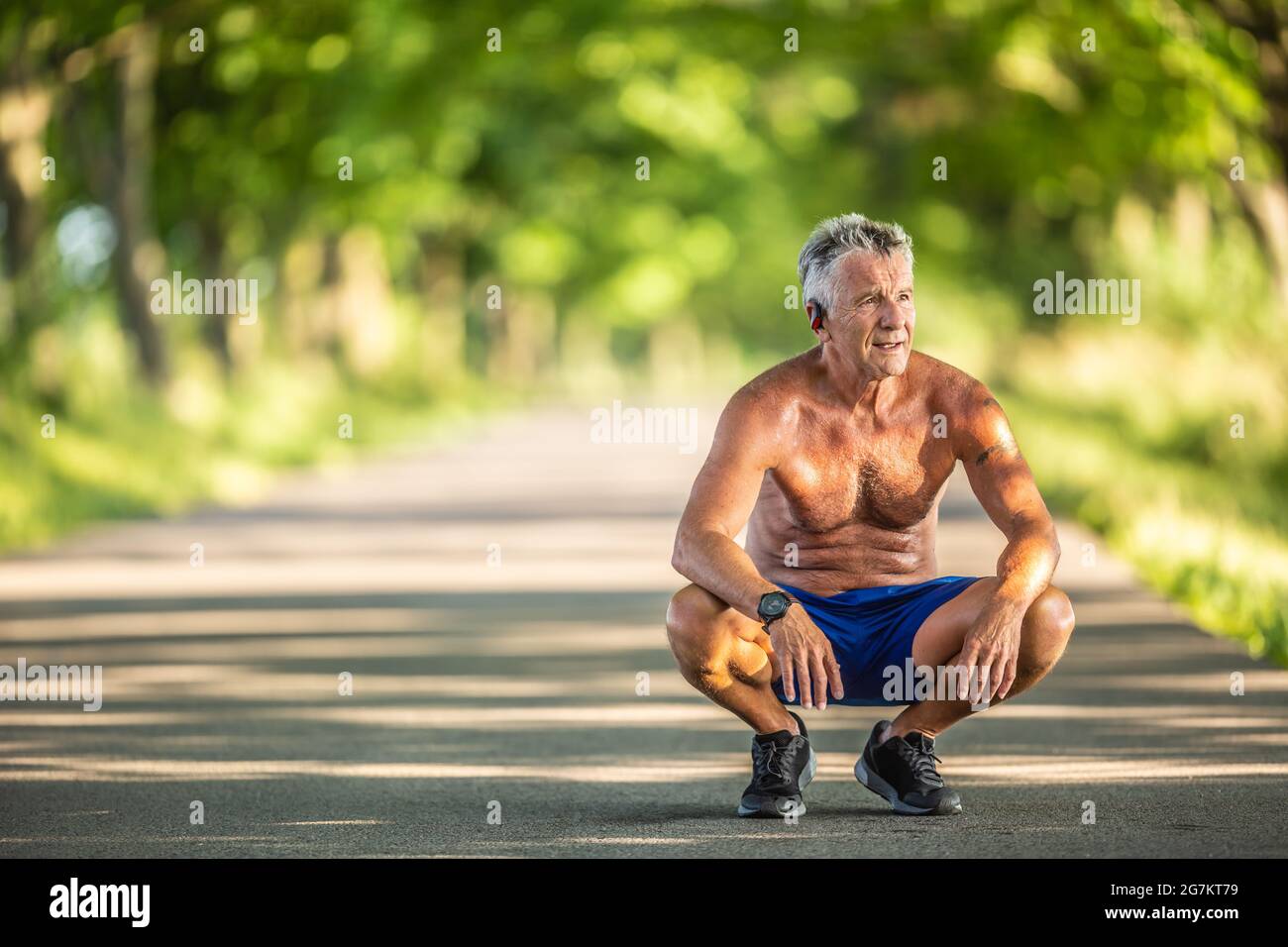 Muskulös und fit Ältere Mann hockt, wie er nach Sport im Freien in der Natur ruht. Stockfoto