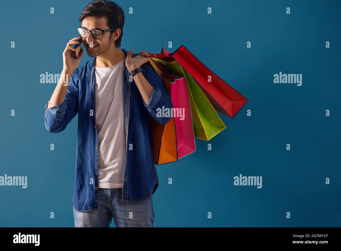 Ein junger Mann, der mit Tragetaschen steht, während er auf dem Handy spricht. Stockfoto