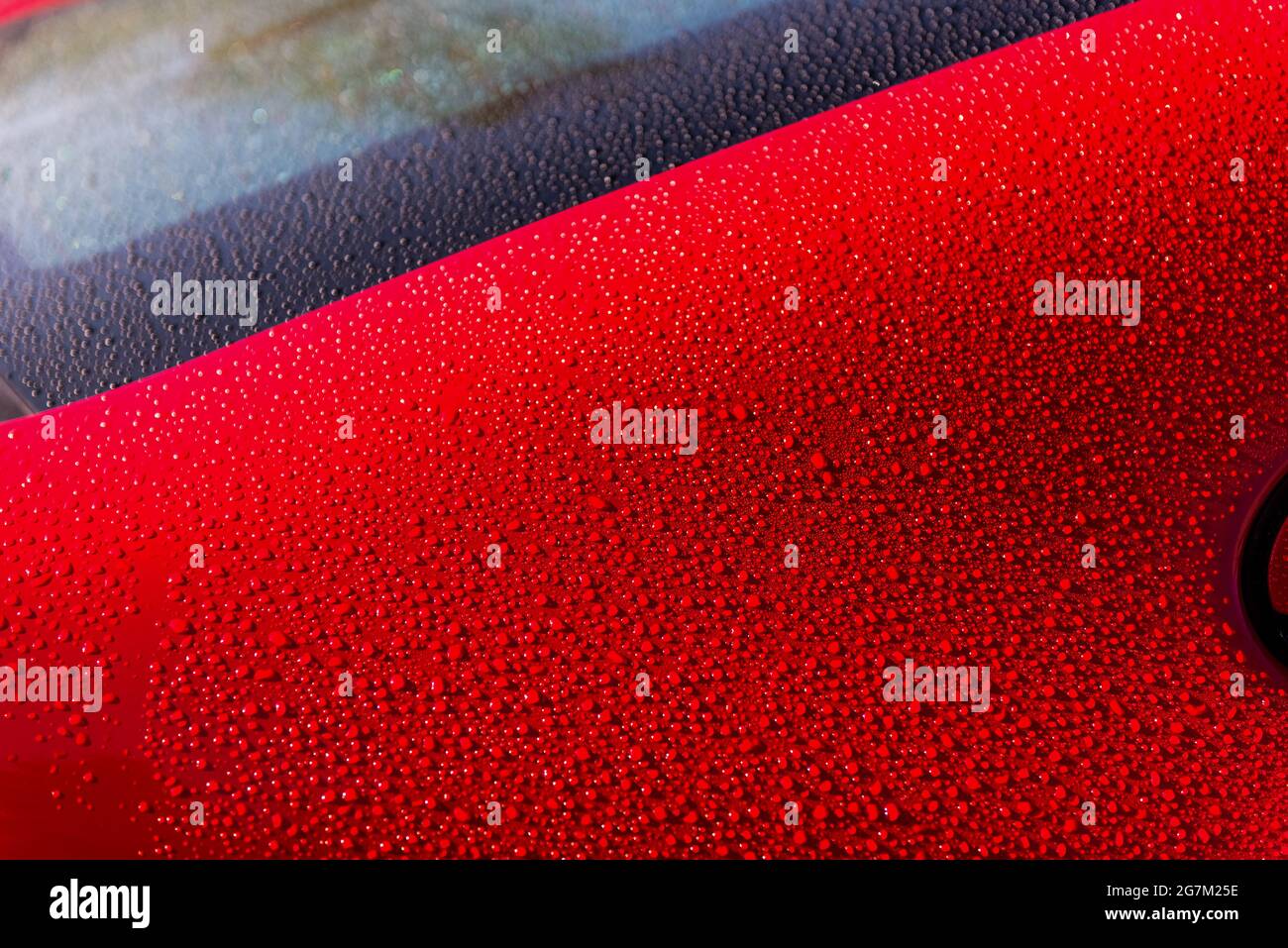 Wassertropfen auf das Auto. Wasser nach Regen oder Autowäsche auf rot glänzender Lackoberfläche abperlt. Hintergrund des Wassertropfens. Wassertropfen-Makro auf einer roten Oberfläche. Stockfoto