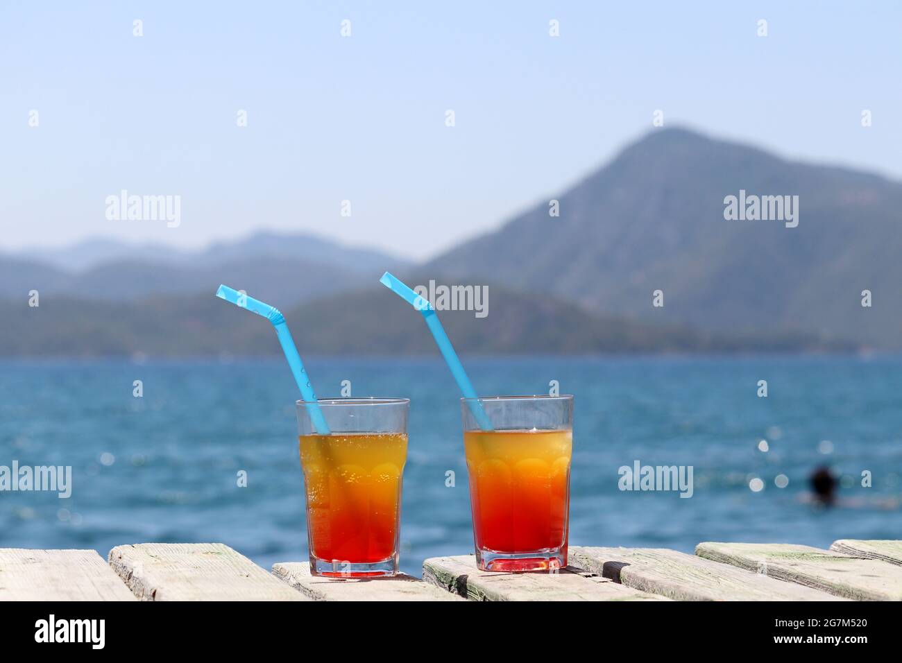 Zwei Gläser mit Cocktail auf einem hölzernen Pier im Meer- und Berghintergrund. Sommerurlaub an einem Strandresort Stockfoto