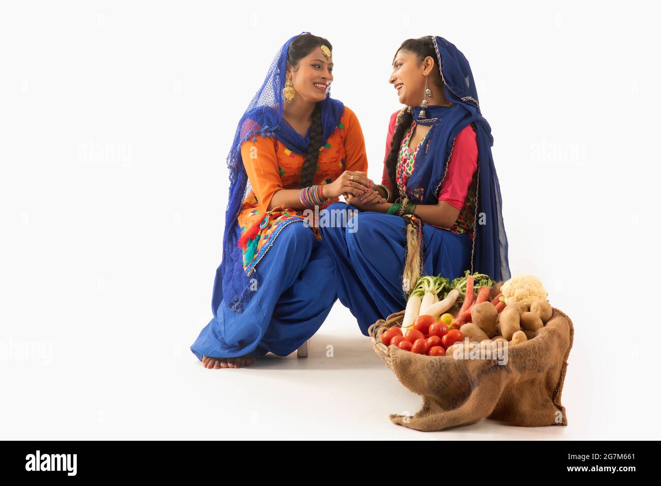 Zwei Frauen im Giddha Kostüm sitzen zusammen und halten Hände mit einem Gemüskorb an ihrer Seite. Stockfoto