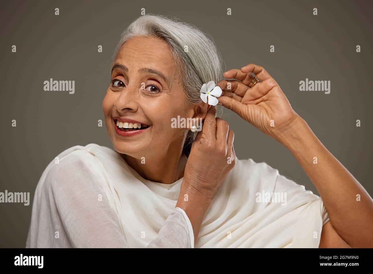 Porträt einer alten schönen Frau, die ihr Haar mit einer Blume anbetend. Stockfoto