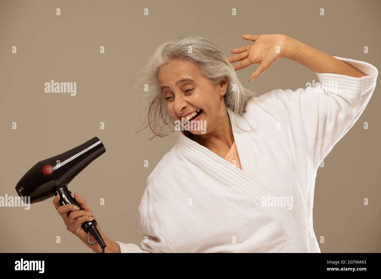 Eine glückliche alte Frau trocknete ihre Haare mit einem Fön. Stockfoto