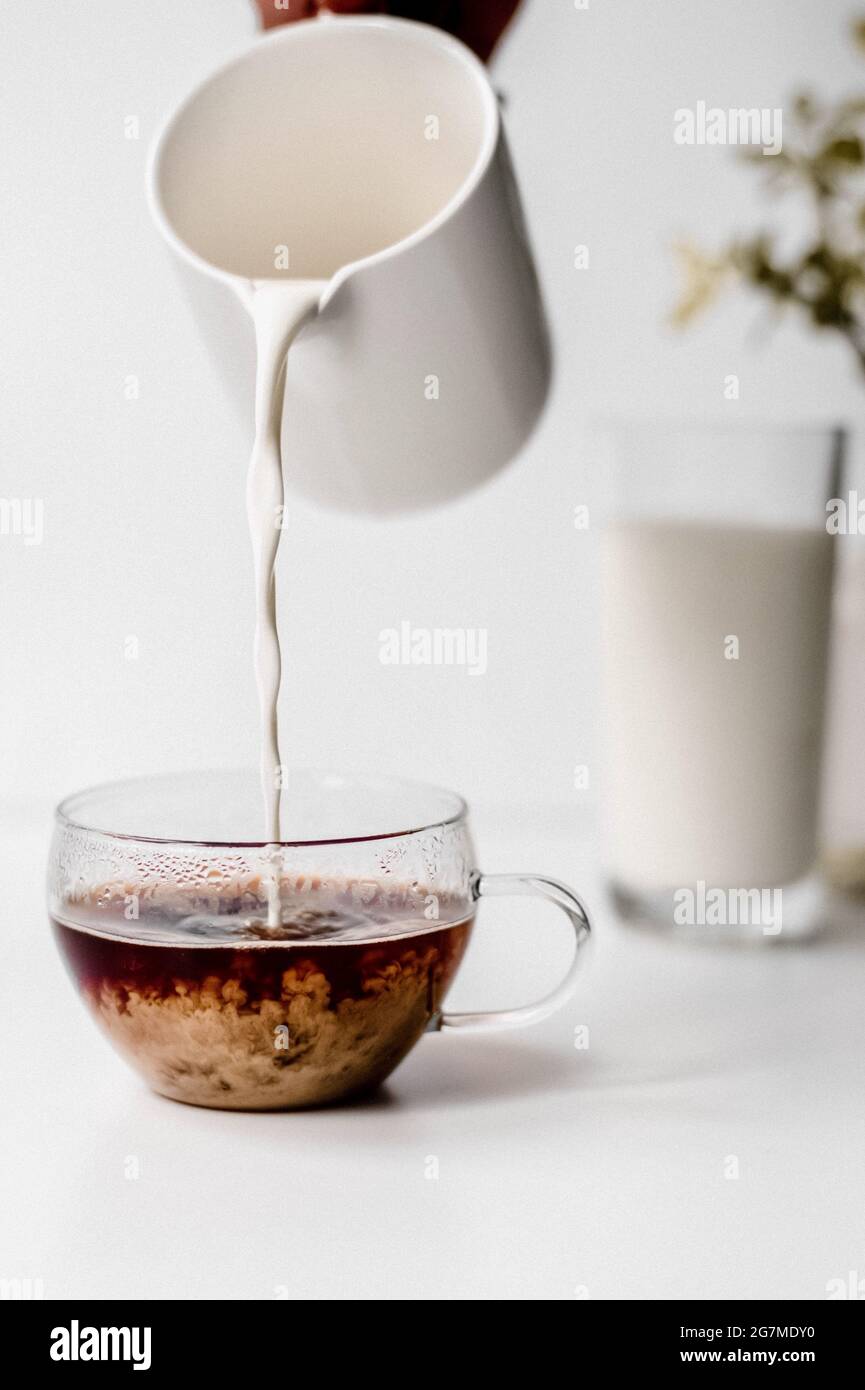 Vertikale Aufnahme einer Hand, die Milch auf einen Kaffee gießt Stockfoto