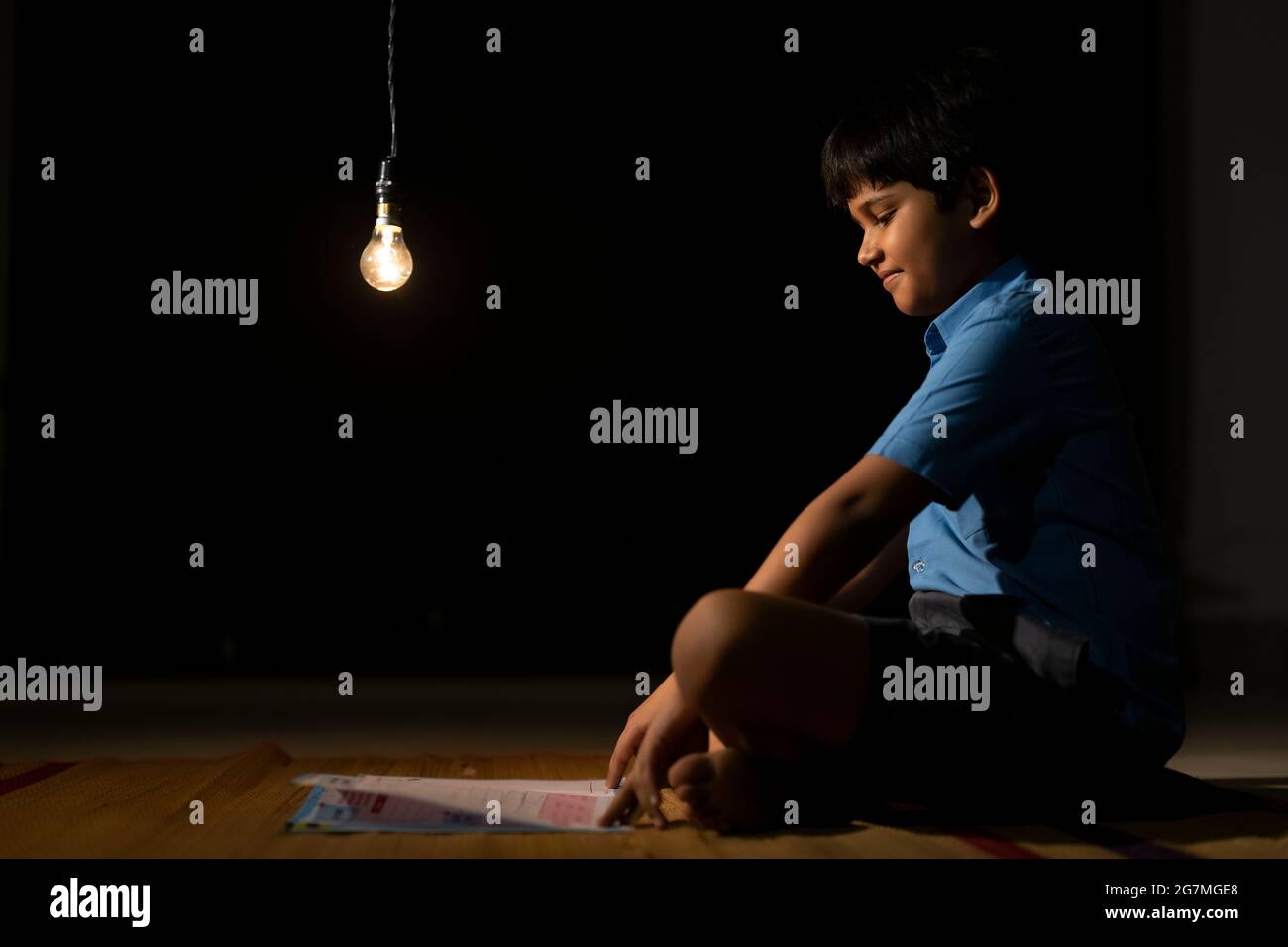 PORTRÄT EINES LÄNDLICHEN JUNGEN, DER NACHTS UNTER GLÜHBIRNENLICHT STUDIERT Stockfoto