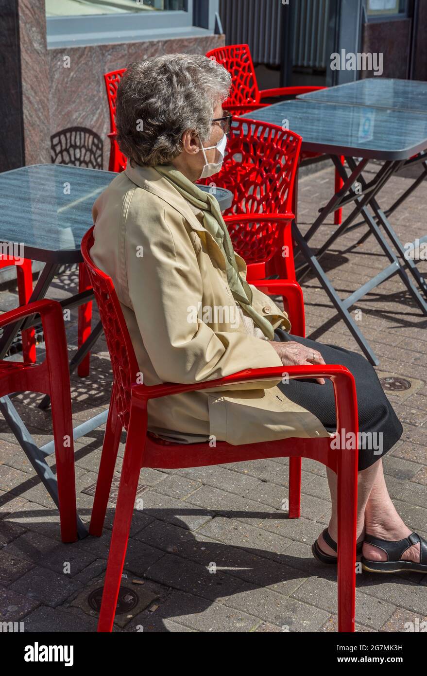 Ältere Frau mit Gesichtsmaske auf Café-Stuhl sitzend - Brüssel, Belgien. Stockfoto
