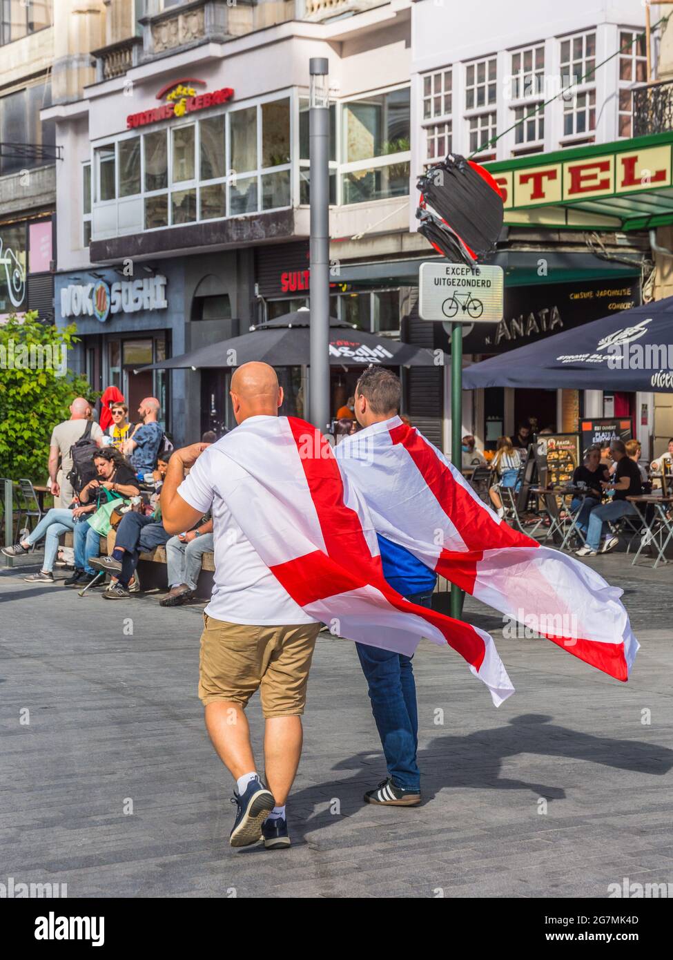 Zwei britische Fußballfans der Euro 2021, die mit der Flagge von St. George über den Schultern durch die Brüsseler Innenstadt laufen Stockfoto