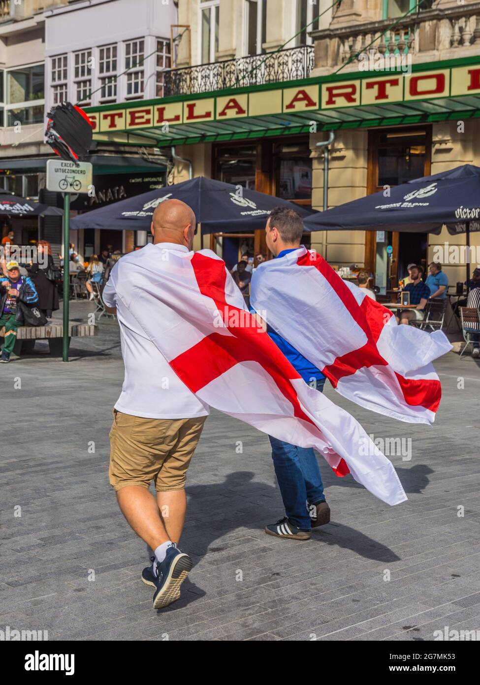 Zwei britische Fußballfans der Euro 2021, die mit der Flagge von St. George über den Schultern durch die Brüsseler Innenstadt laufen Stockfoto