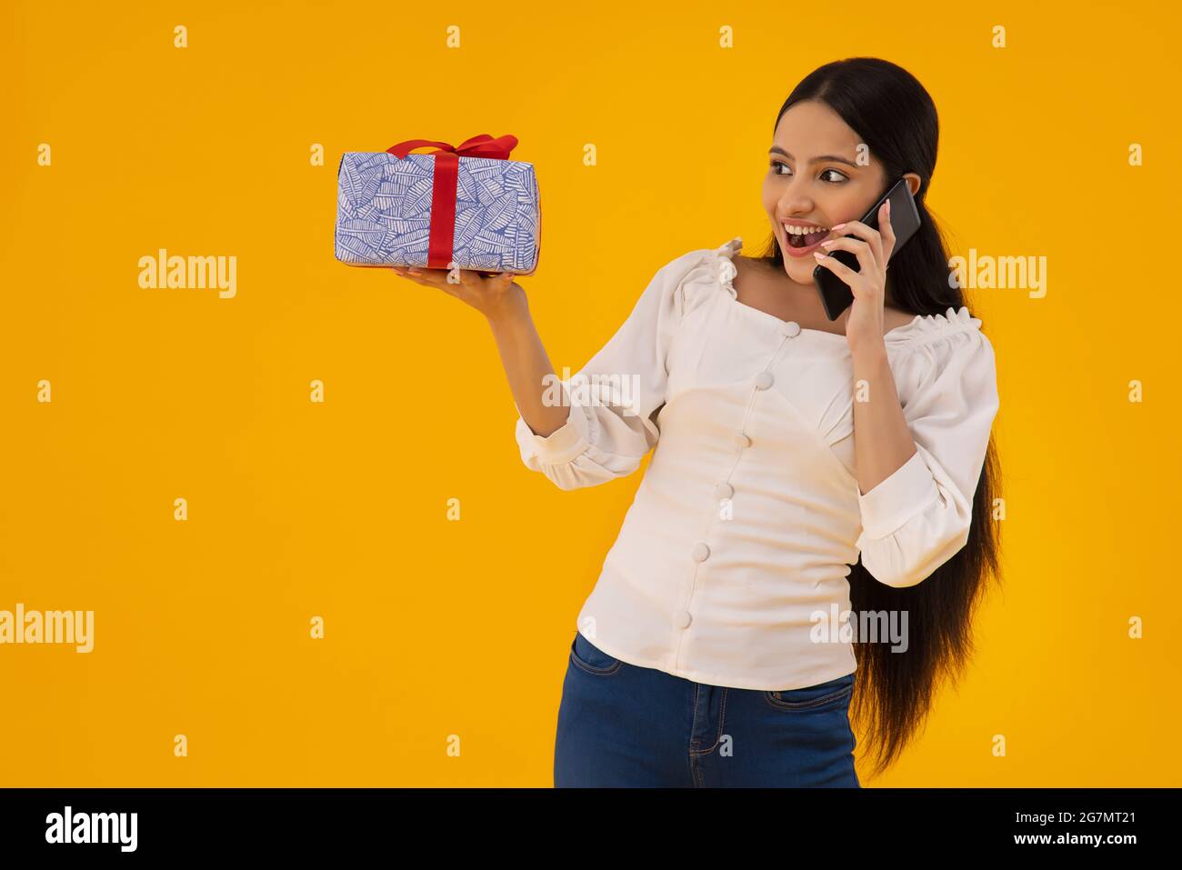 Eine Frau mit einem Geschenk in der Hand, die telefoniert. Stockfoto
