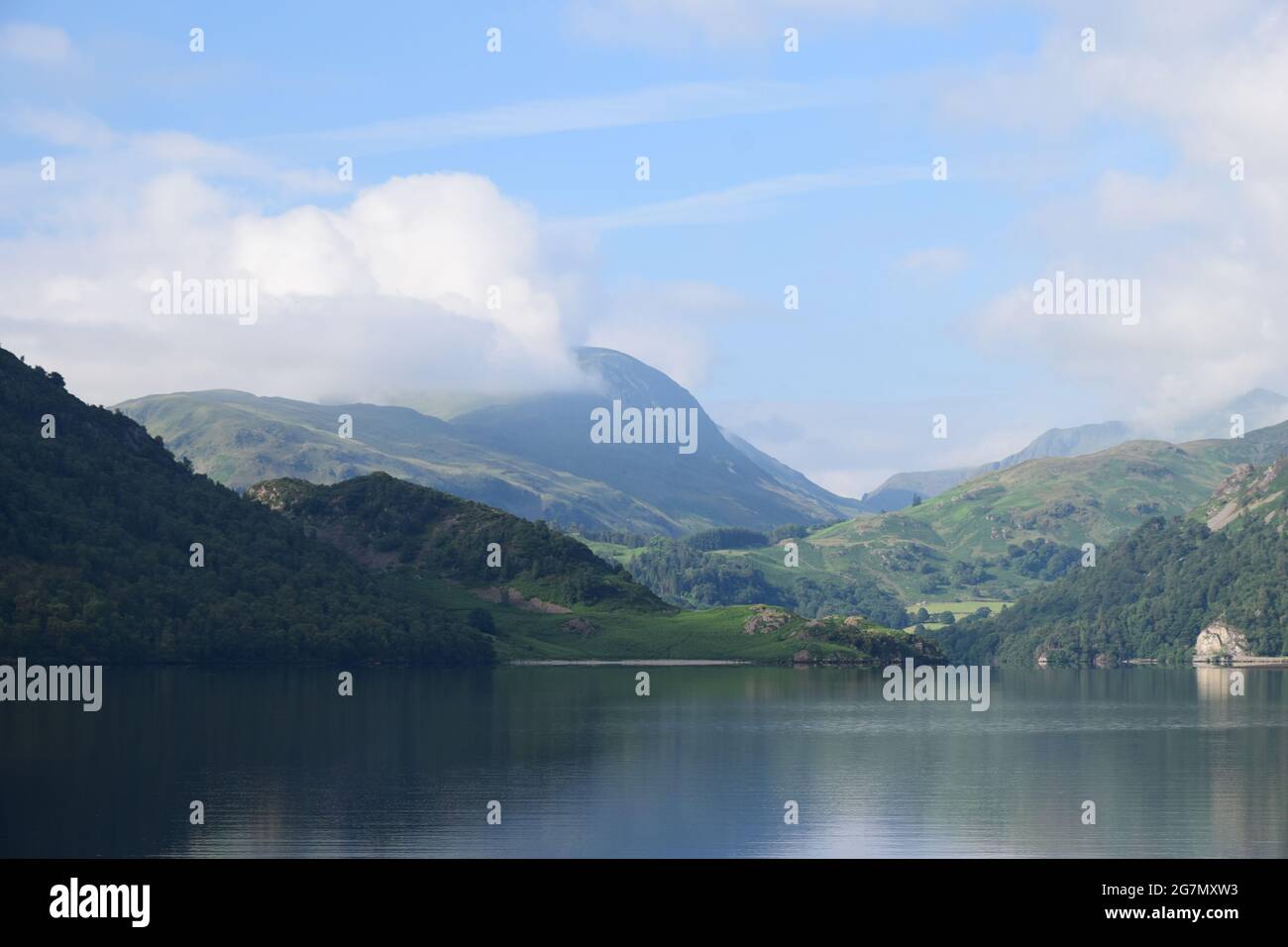 Ullswater im Seengebiet wurde am frühen Morgen eines Sommertages aufgenommen, wobei die umliegenden Hügel und der Himmel sich von seiner ruhigen Oberfläche abspiegeln. Stockfoto